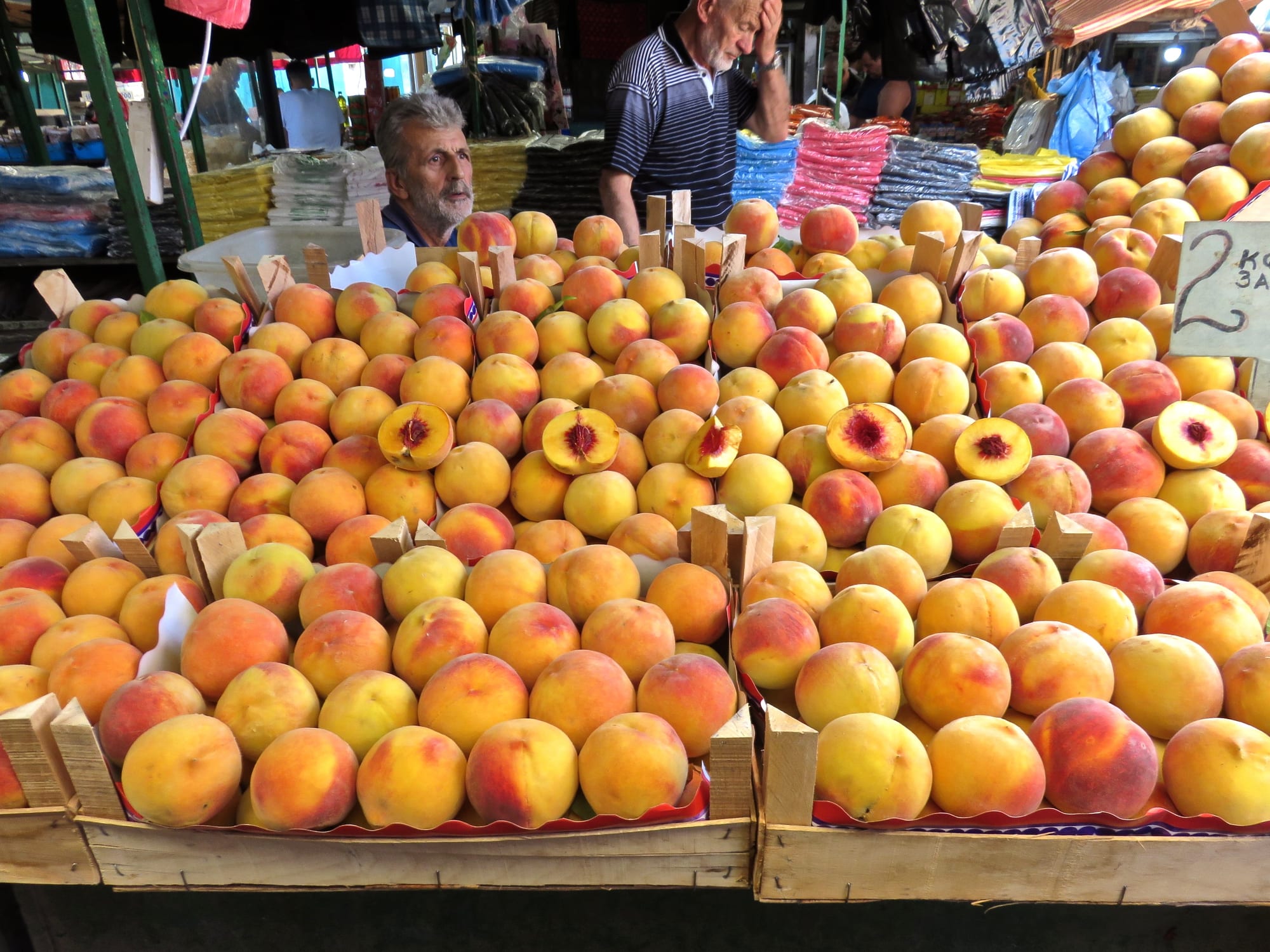 Crates of peaches piled high at an outdoor market stall, with a vendor standing behind them