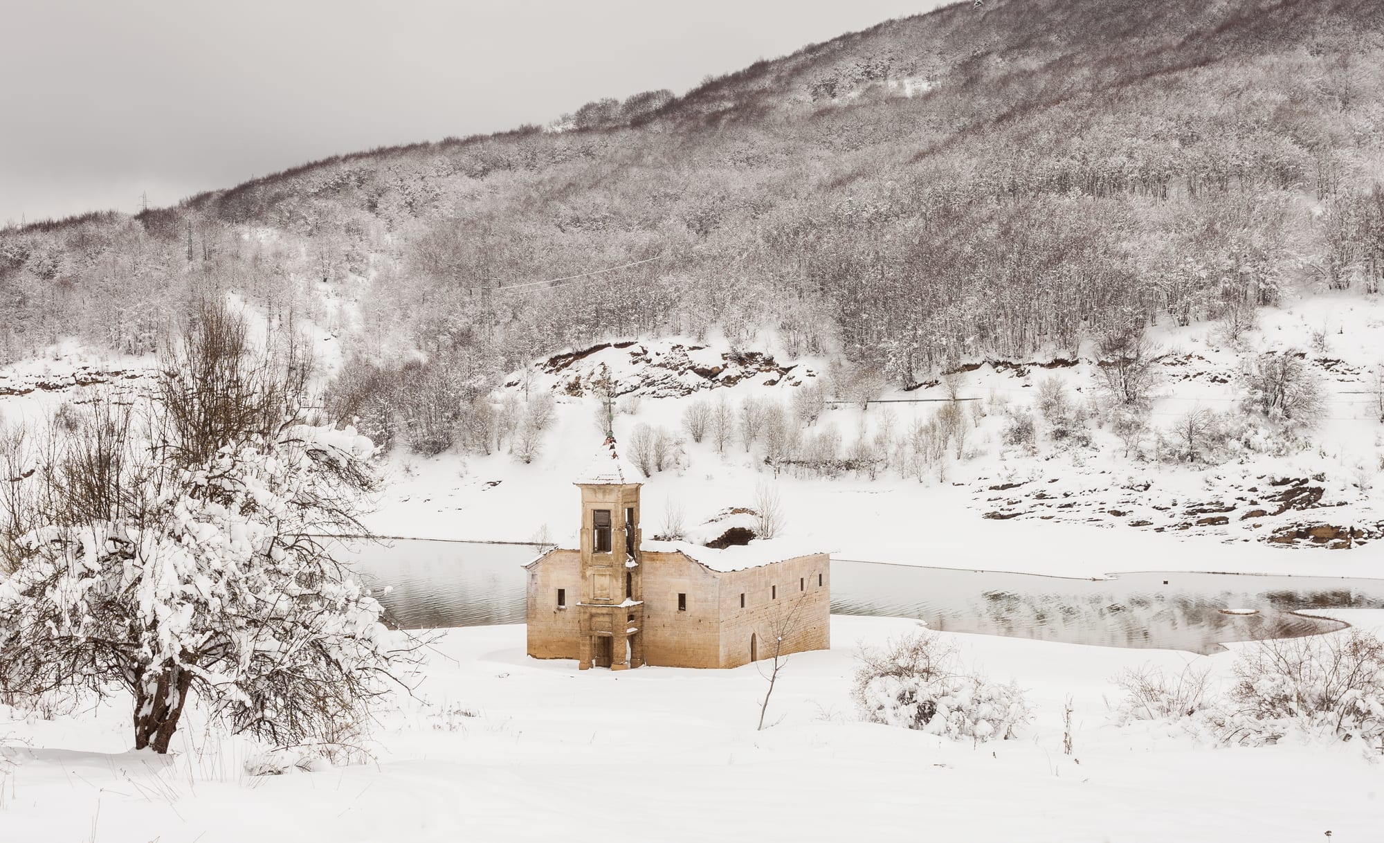 A small church tower rising from the shallow waters of a lake
