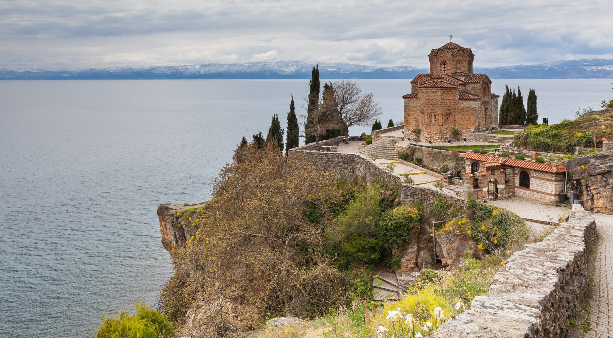 A stone Byzantine church on a headland above a wide, calm lake