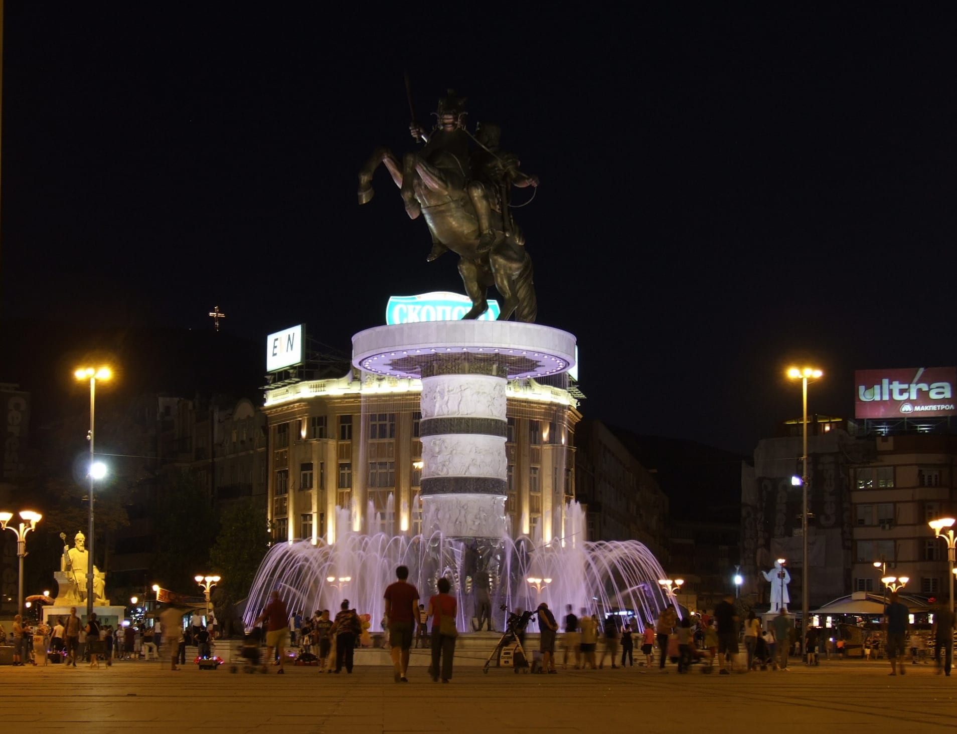 A huge illuminated equestrian statue on a tall column in a city square at night