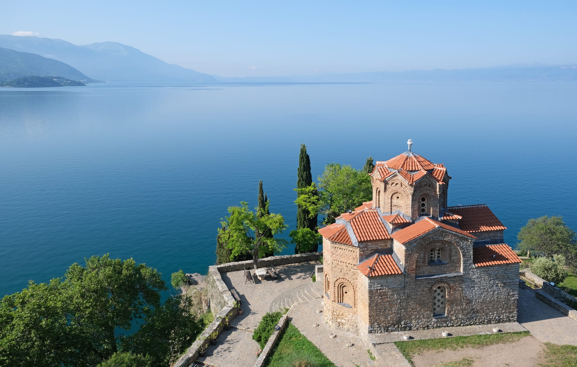 A small stone church on a cliff edge above a deep blue lake