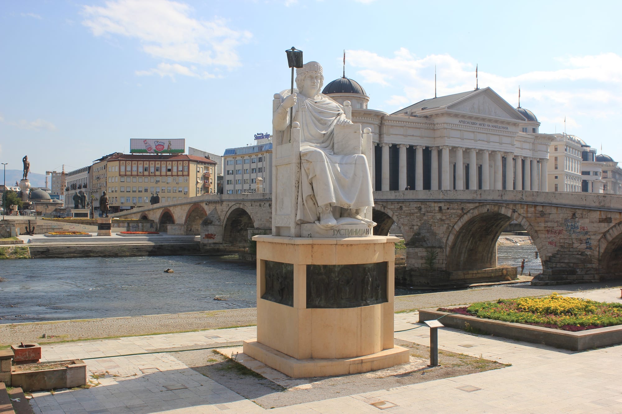 An old stone arched bridge crossing the Vardar river in Skopje, with the old bazaar and a fortress behind