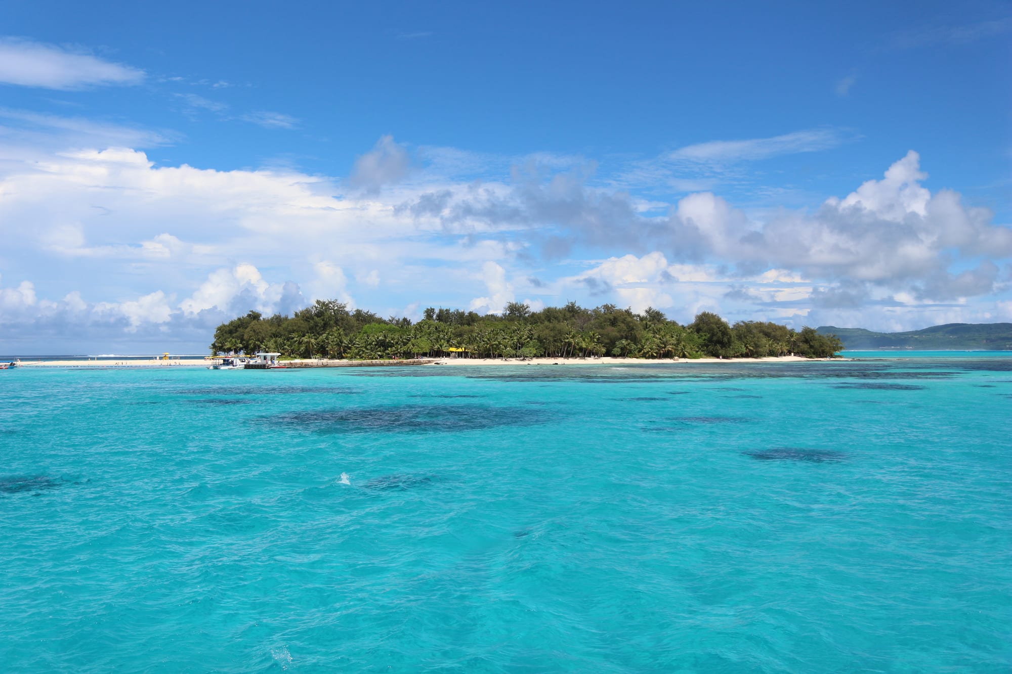 A small round island of white sand and palm trees surrounded by turquoise water
