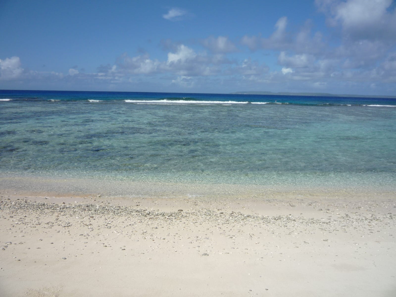 Clear turquoise lagoon water breaking over a reef in front of a white sand beach