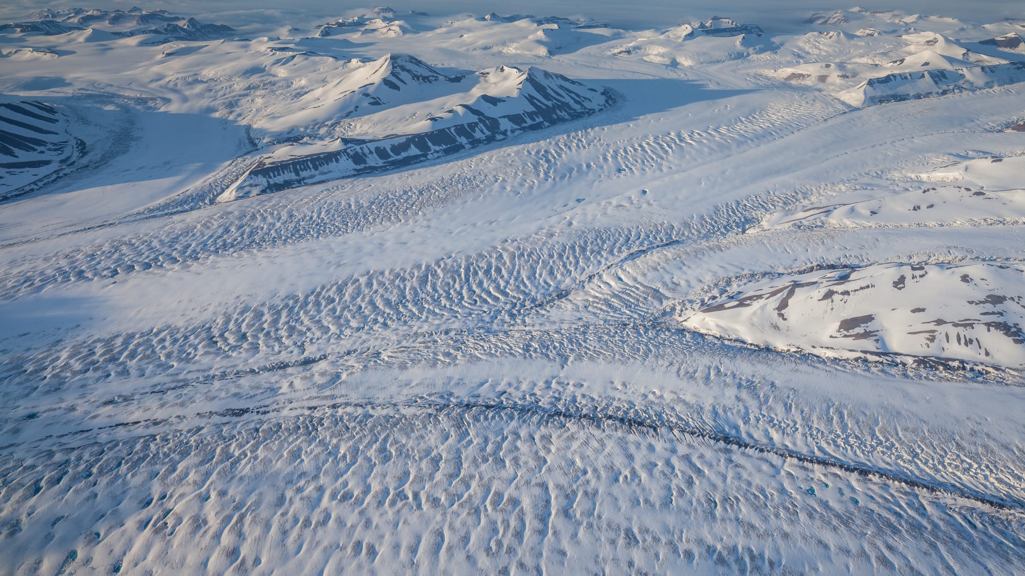 A vast glacier flowing between mountains under the midnight sun