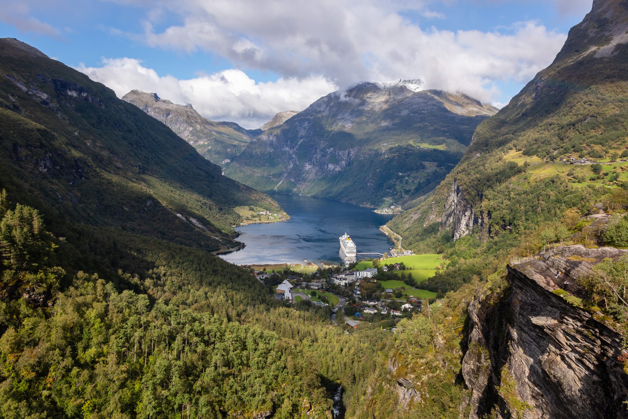 An elevated view over a narrow fjord surrounded by steep mountains and waterfalls