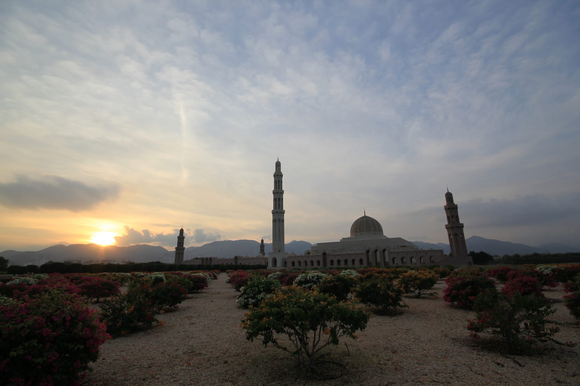A large white mosque with a golden dome and tall minarets set among gardens
