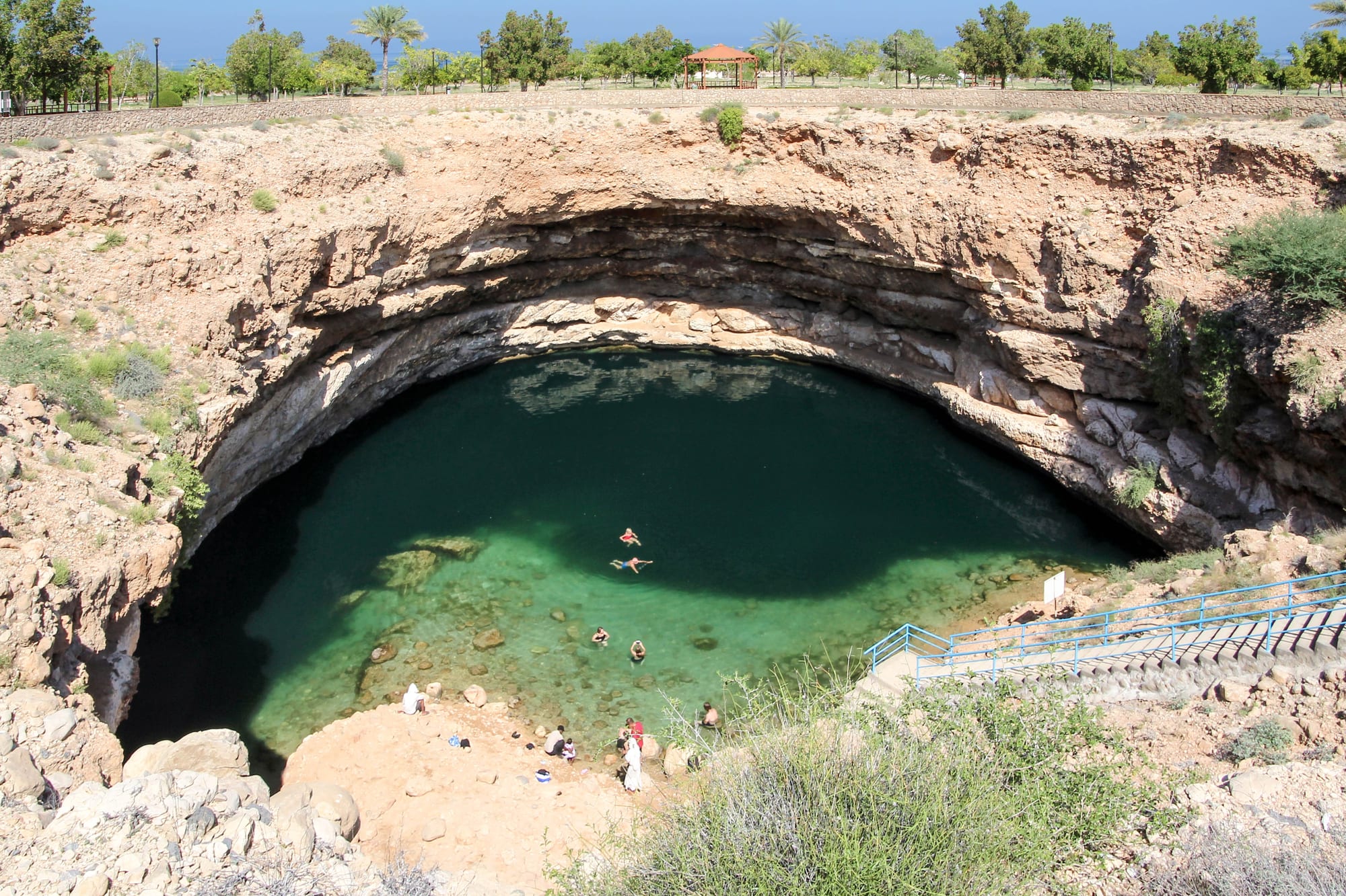A deep circular limestone sinkhole filled with turquoise-green water