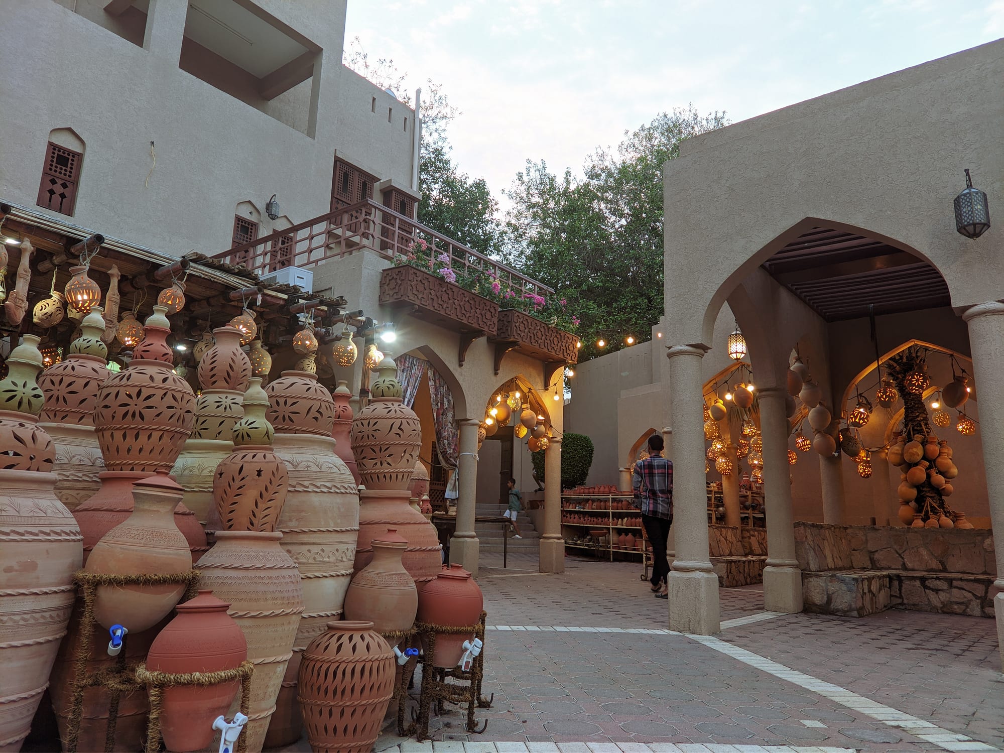 Rows of large earthenware jars and pots with carved patterns stacked in a market courtyard, with pierced clay lanterns glowing under arched walkways