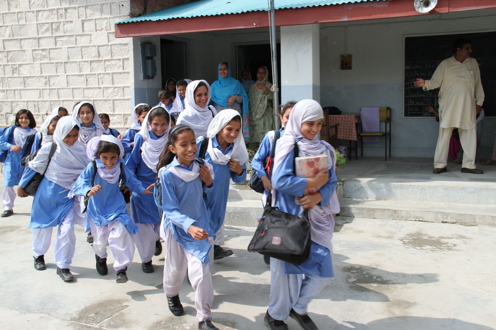 A group of schoolgirls in blue and white shalwar kameez uniforms walking and playing outside a school building