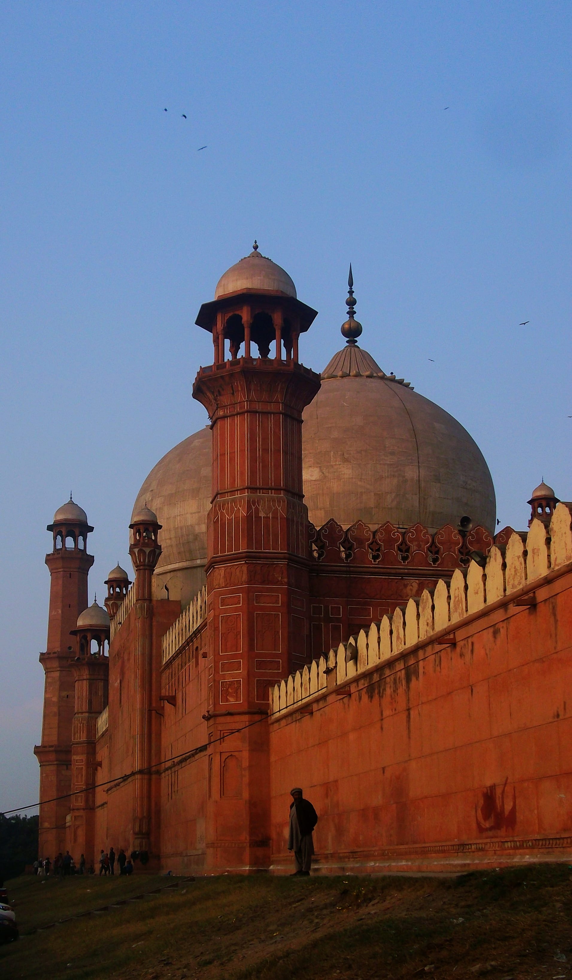A grand red sandstone mosque with large white domes and minarets at dusk