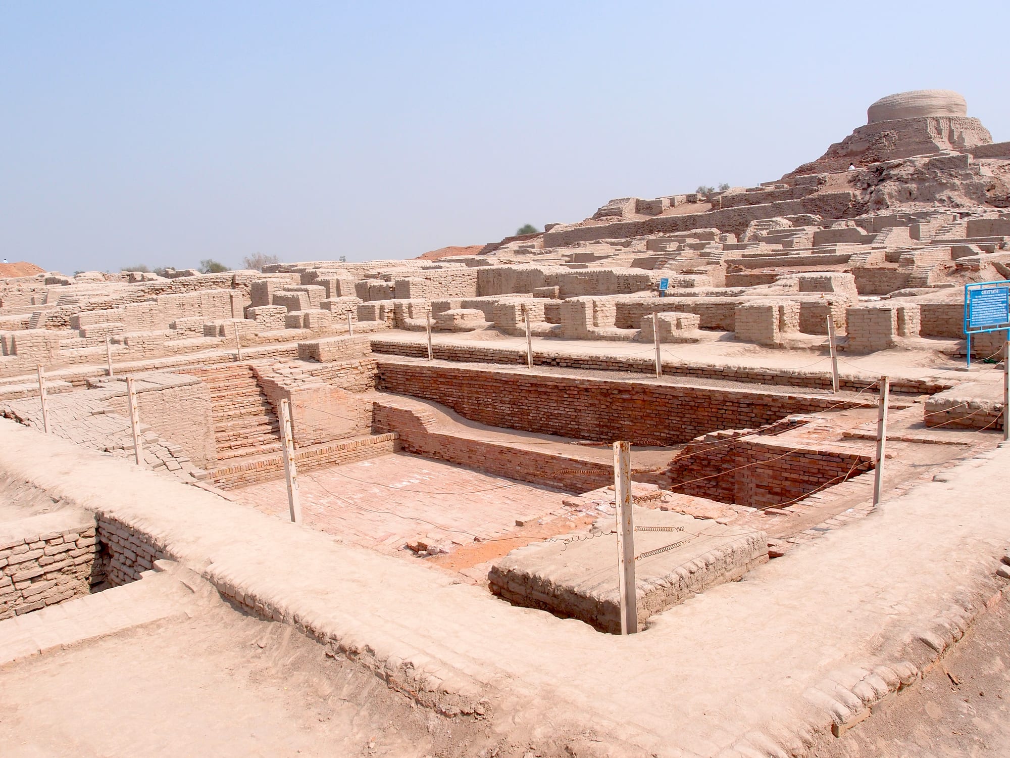 The excavated brick ruins of an ancient city with a stupa mound in the background