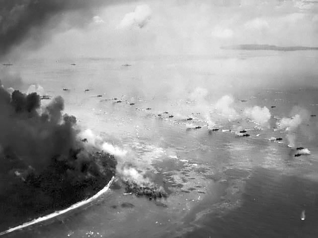 A line of amphibious tracked landing vehicles heading through the surf toward a smoke-covered beach at Peleliu in 1944