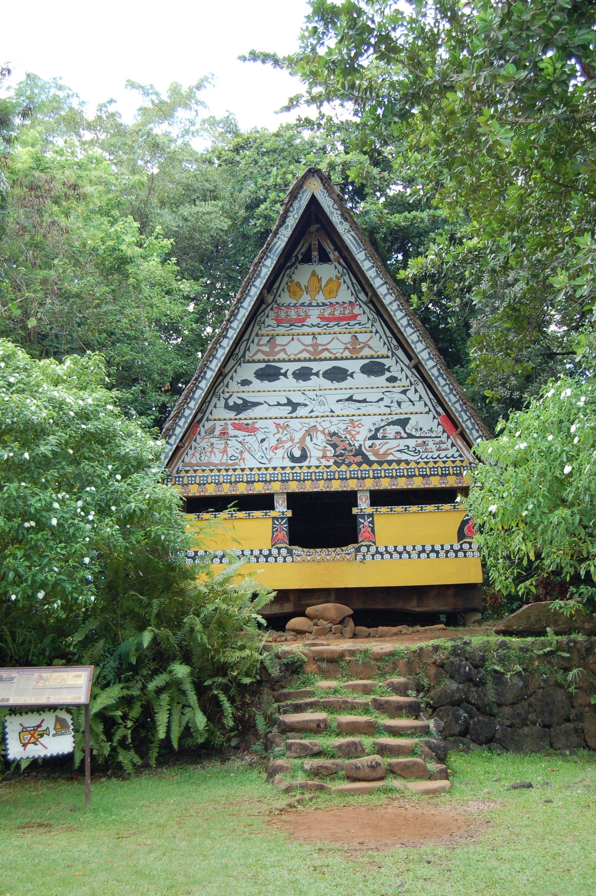 A traditional Palauan meeting house with a steeply pitched roof and painted gable, raised on a stone platform
