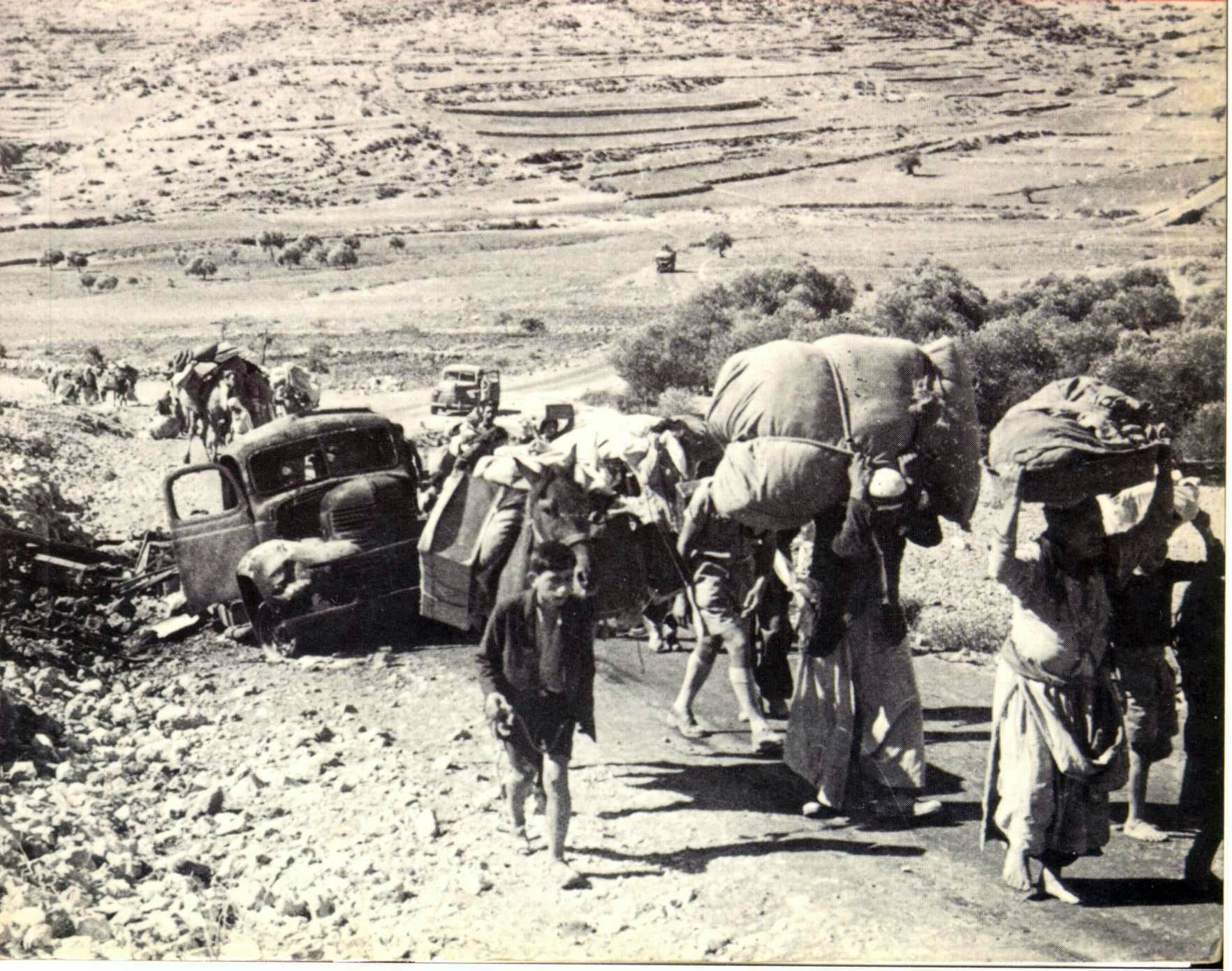 A long column of Palestinian refugees, many carrying bundles, walking along a road in 1948