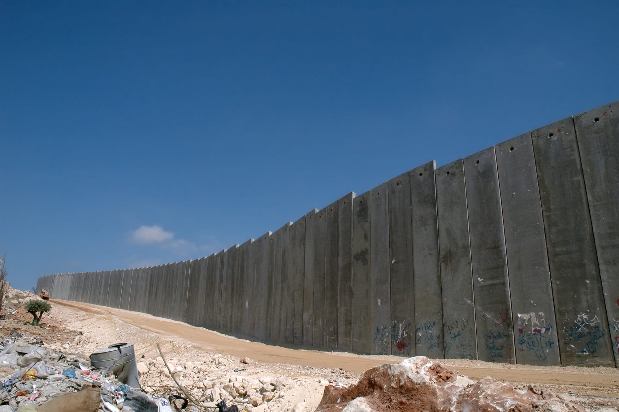 A high concrete wall topped with a watchtower running through a Palestinian urban area in the West Bank