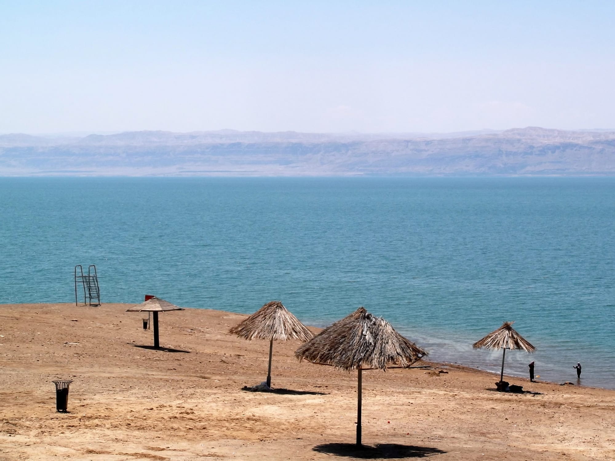 A calm salt lake shoreline with distant hills, under a hazy sky