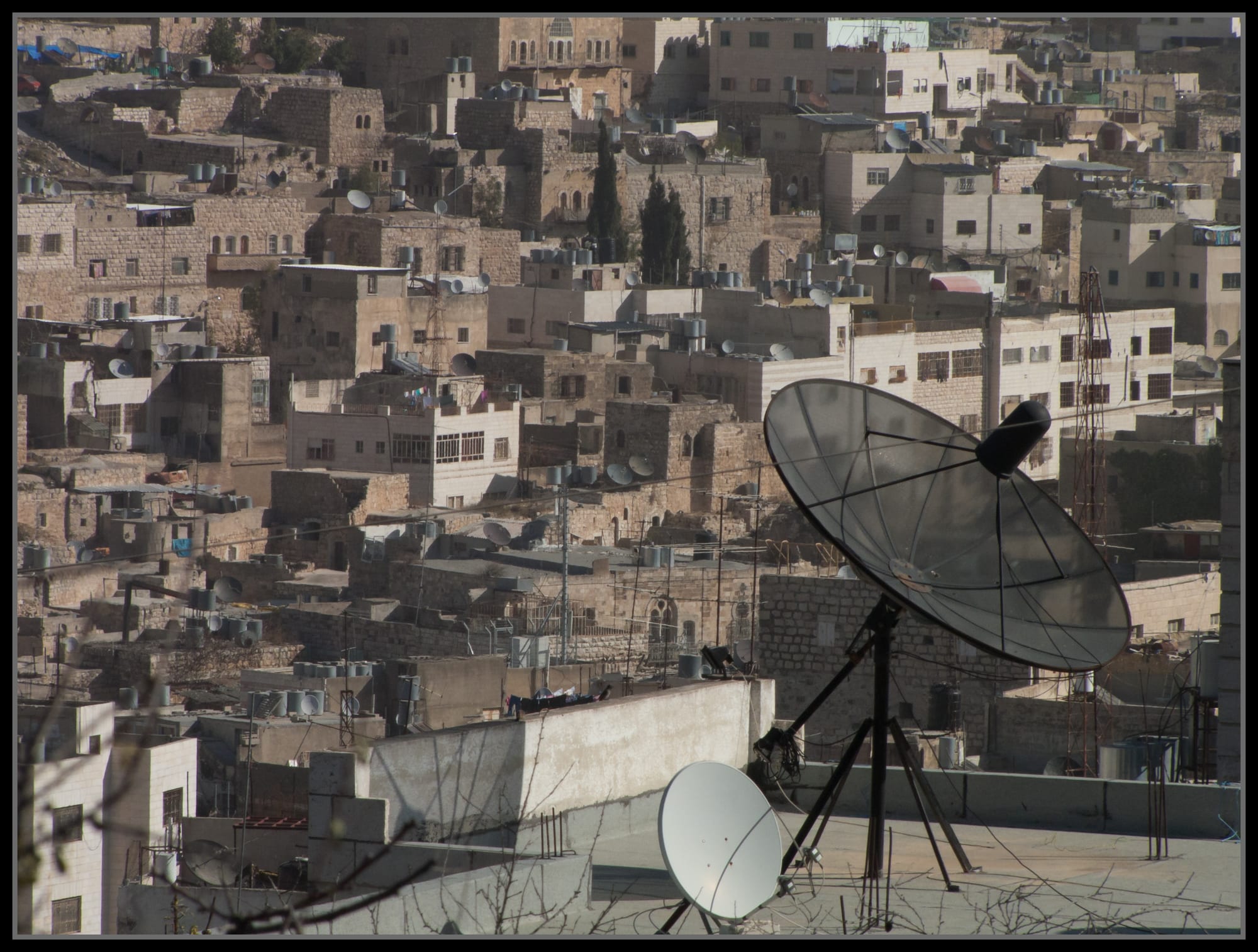A dense hillside of stone houses in Hebron's Old City, rooftops crowded with satellite dishes and water tanks
