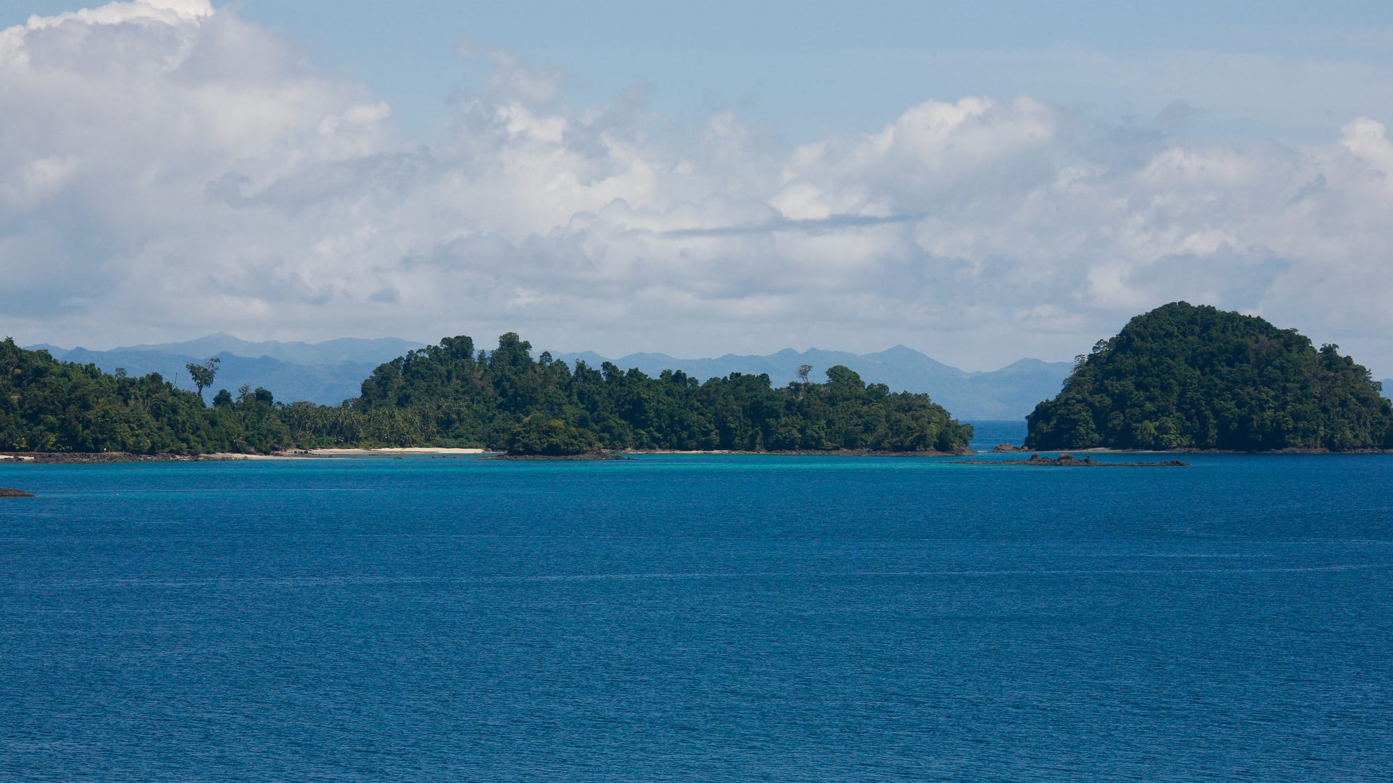 A forested tropical bay with small islands in calm turquoise water