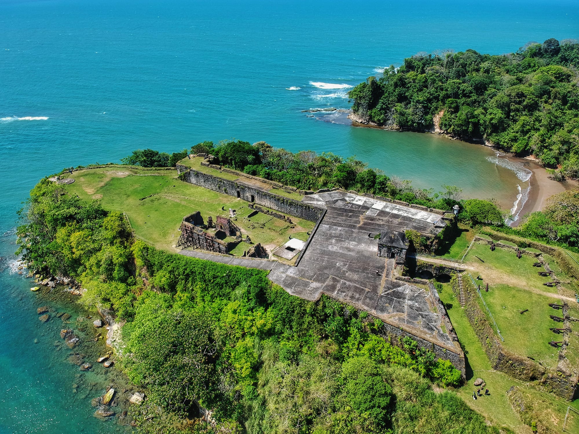 An aerial view of a ruined stone fort on a forested headland above the sea
