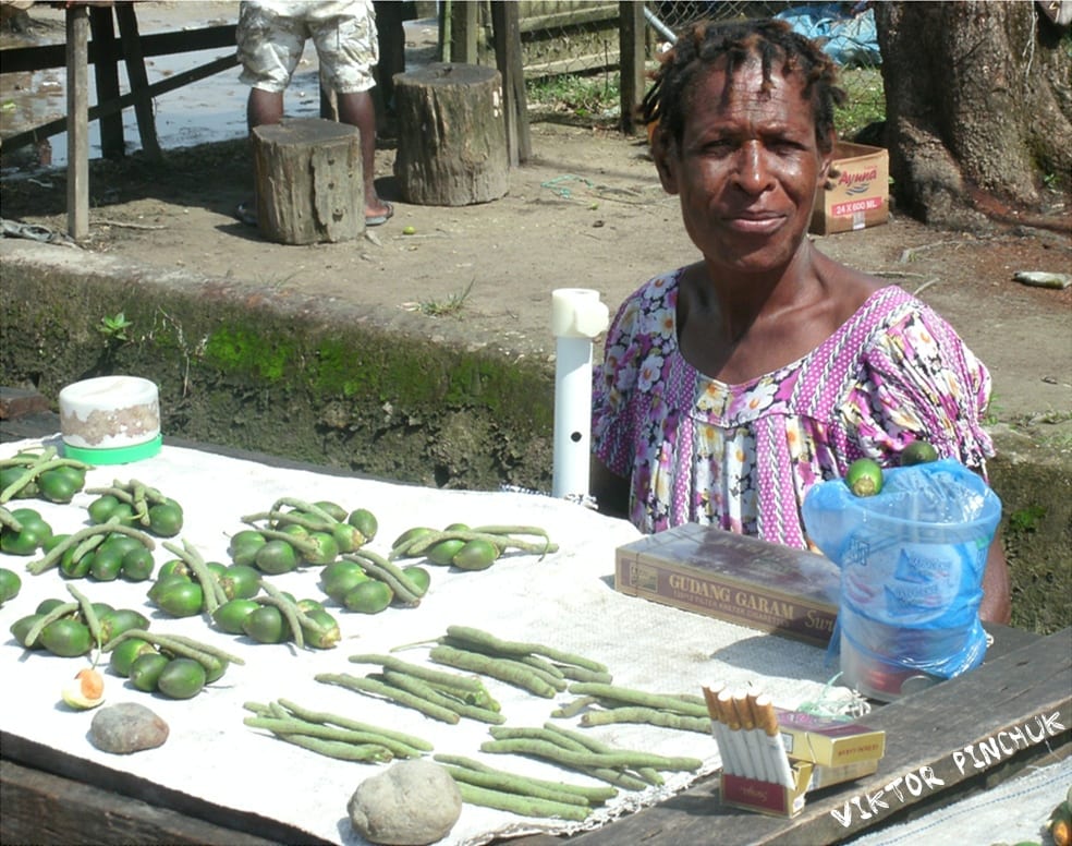 A woman selling betel nut, lime and mustard sticks laid out on a table at a roadside stand