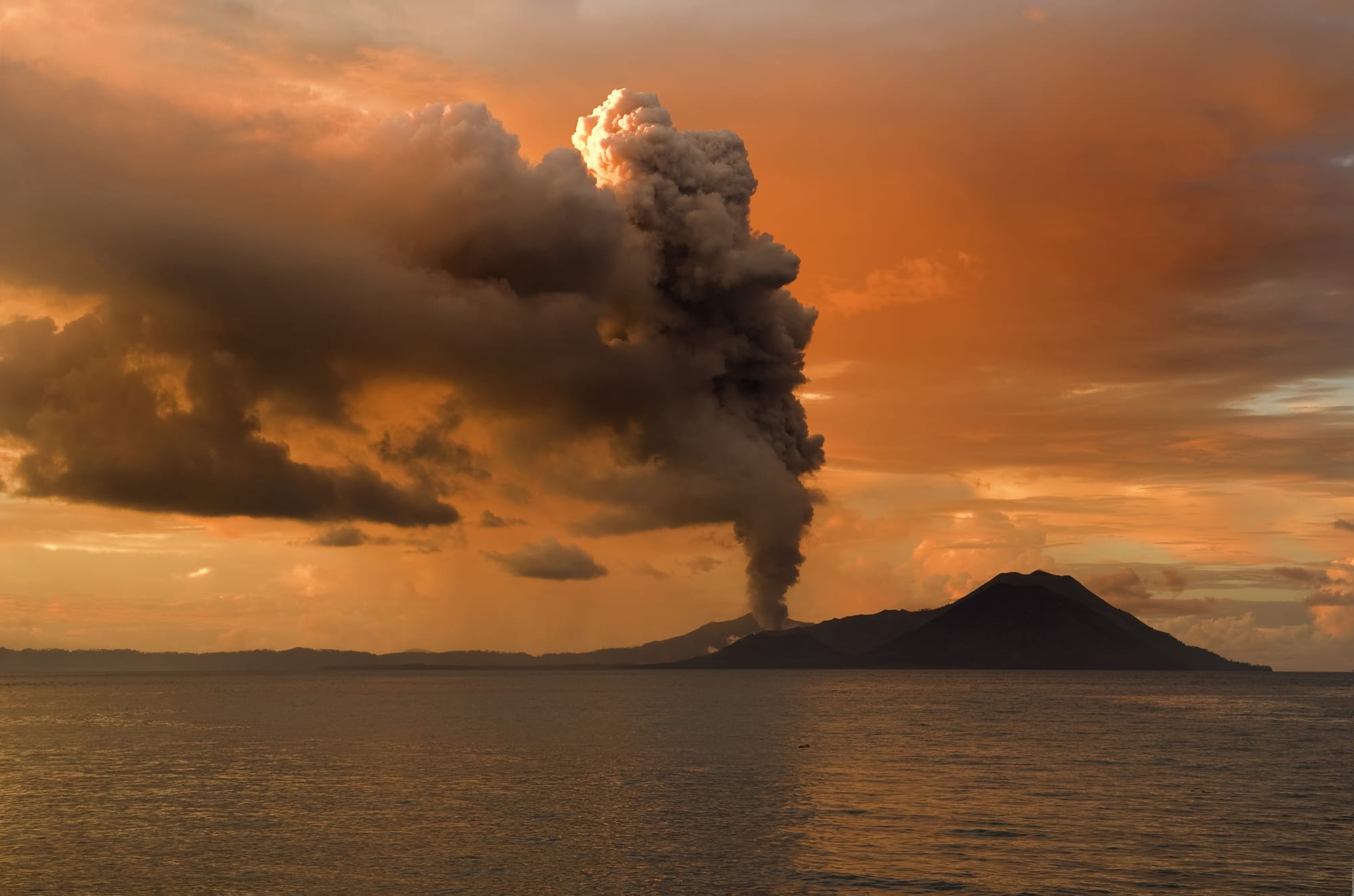 An active volcano venting smoke beside a coastal town