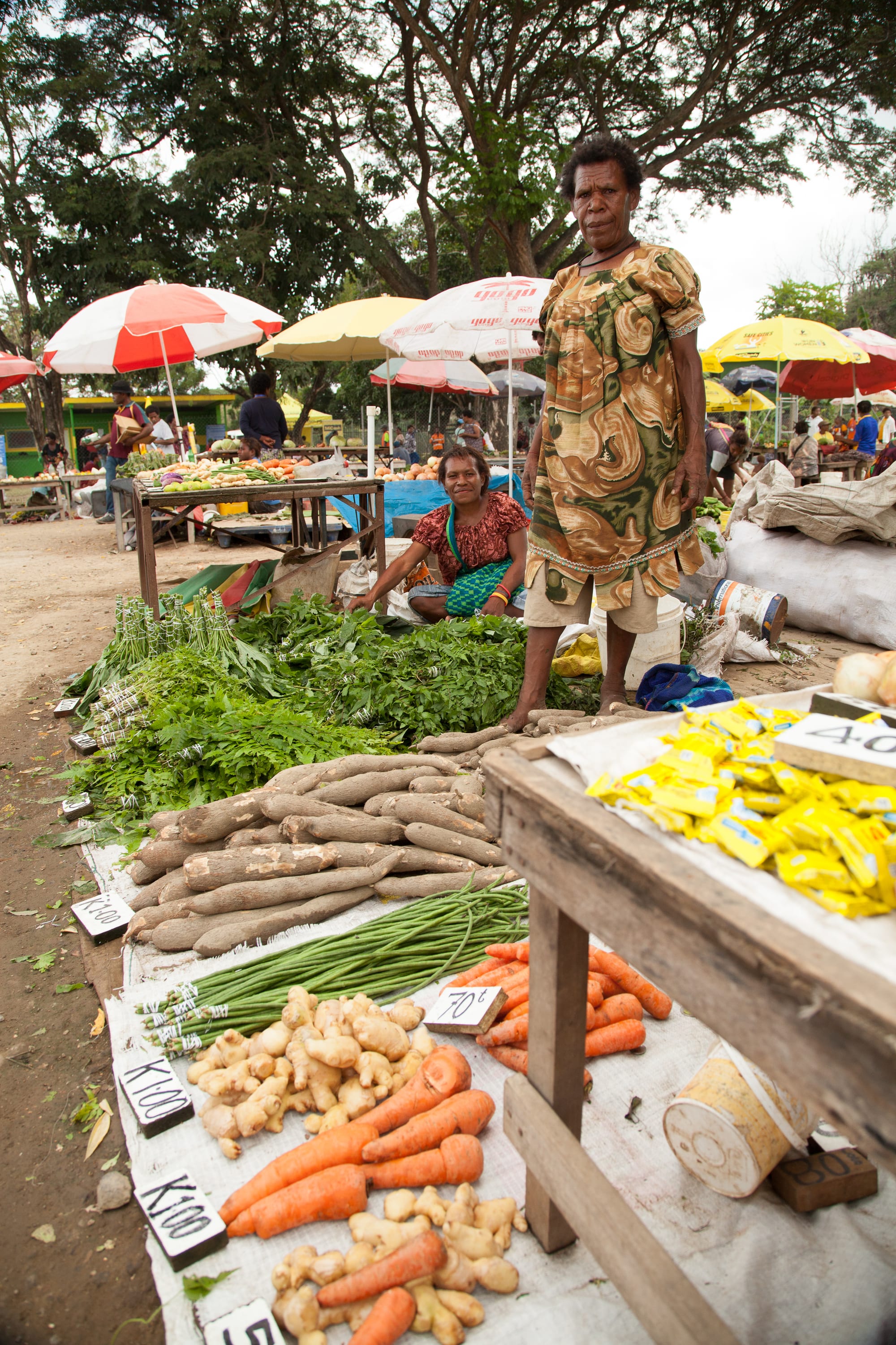 Carrots, sweet potato, ginger and greens laid out for sale at an outdoor market