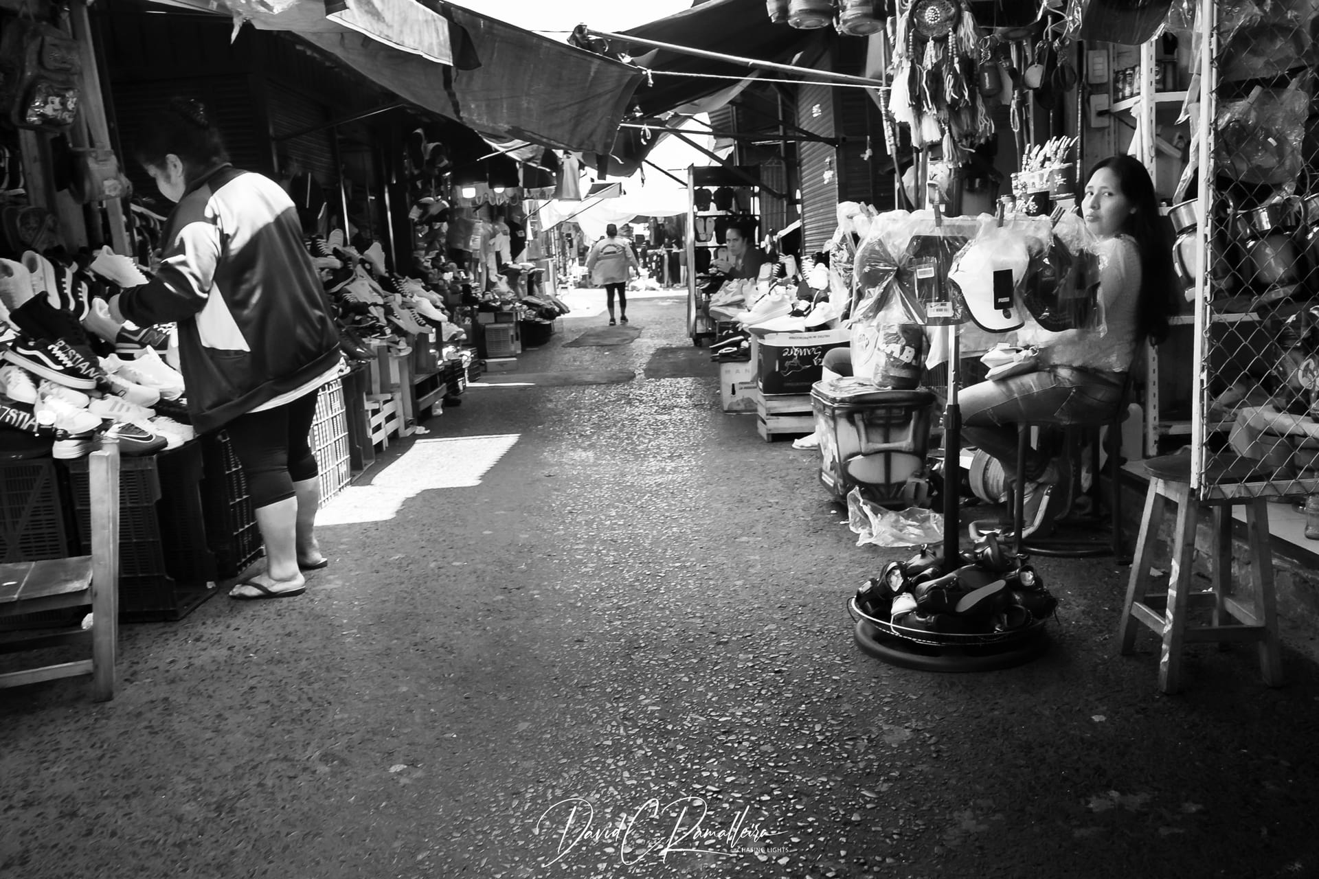 A narrow aisle inside Mercado 4 in Asunción, lined with stalls, a shoe vendor and a seated woman