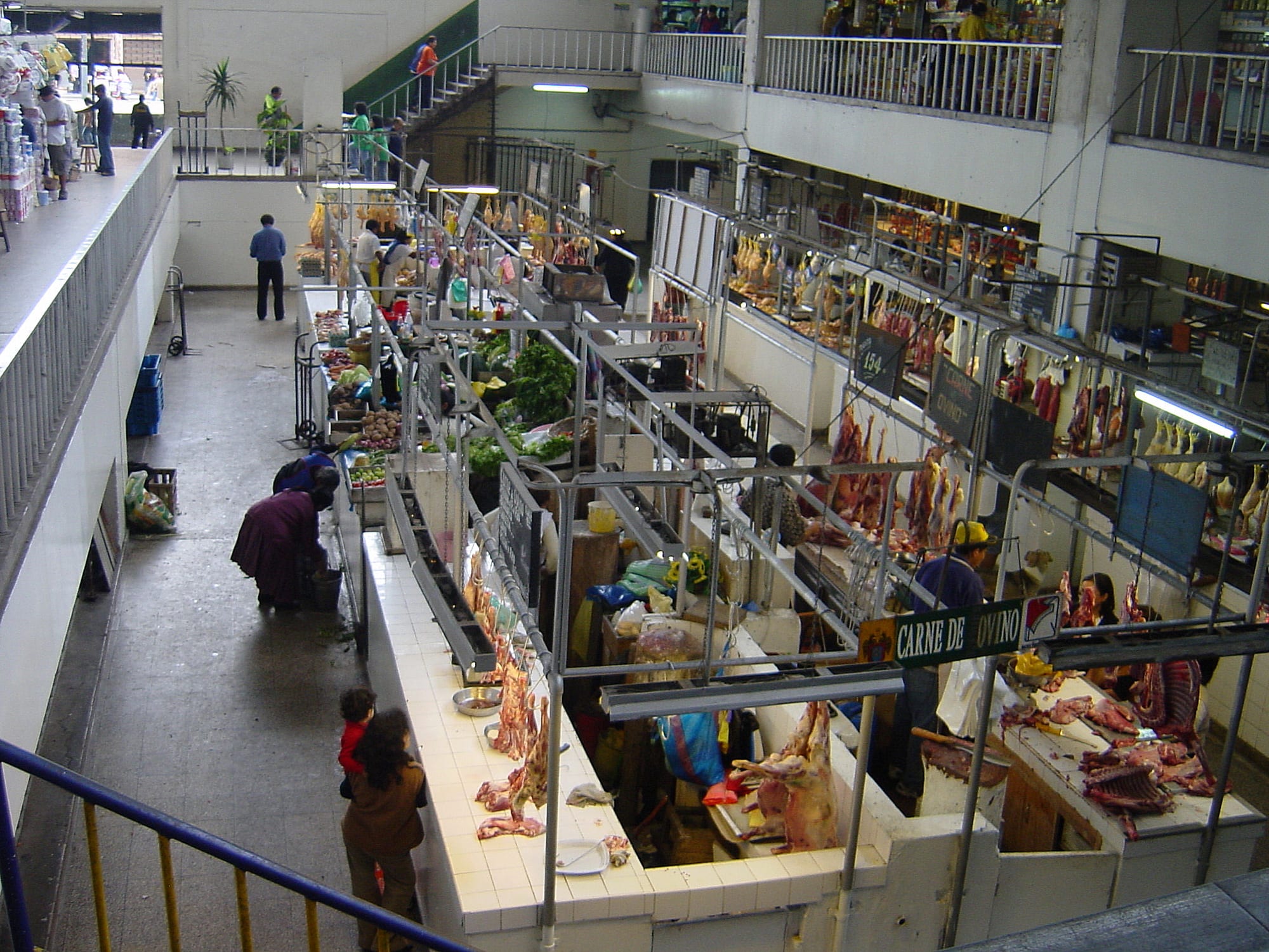 Rows of covered meat and produce stalls seen from an upper walkway inside a busy indoor market in Lima