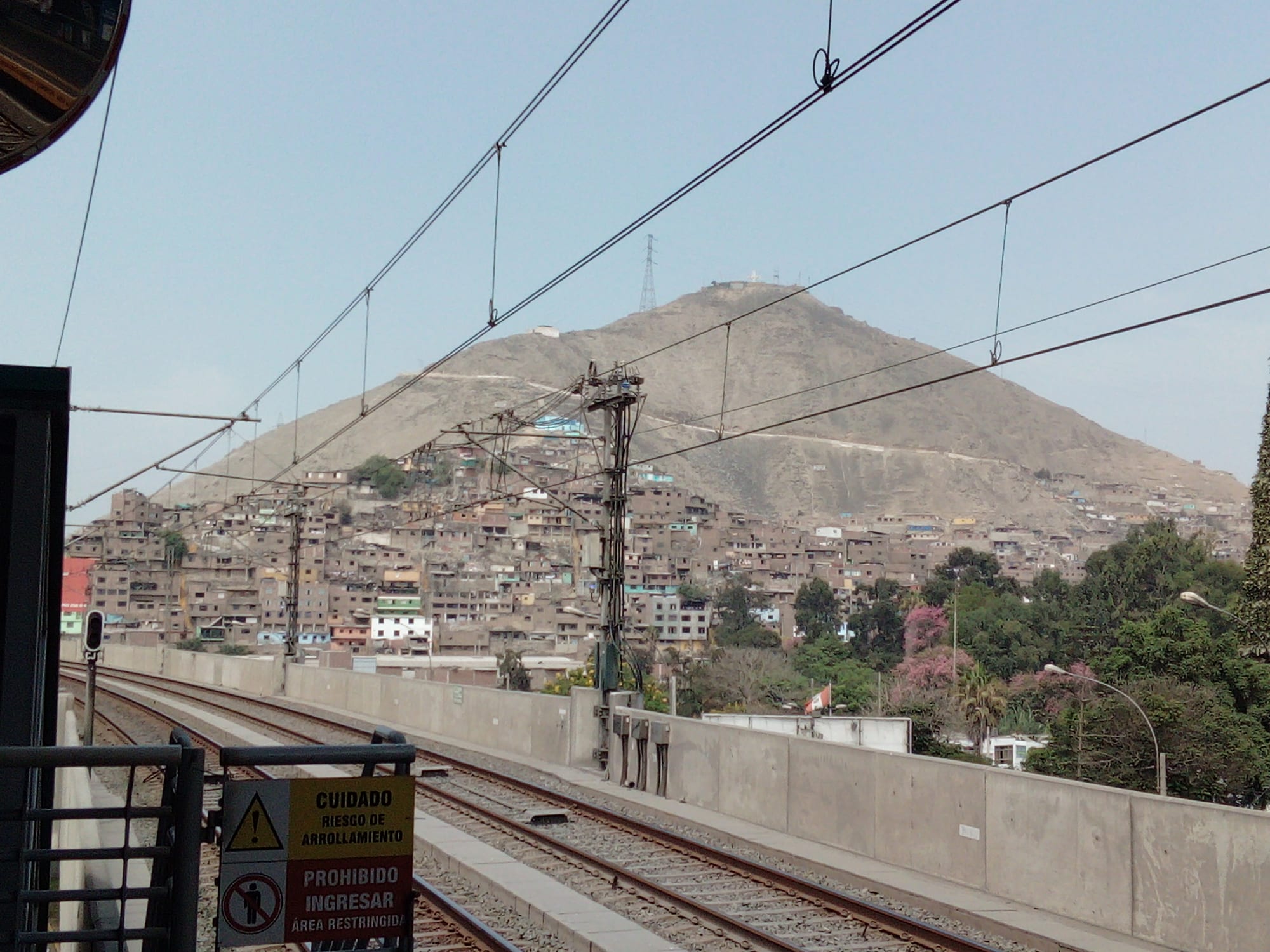 Houses climbing a dry, dusty hillside above train tracks in San Juan de Lurigancho, Lima