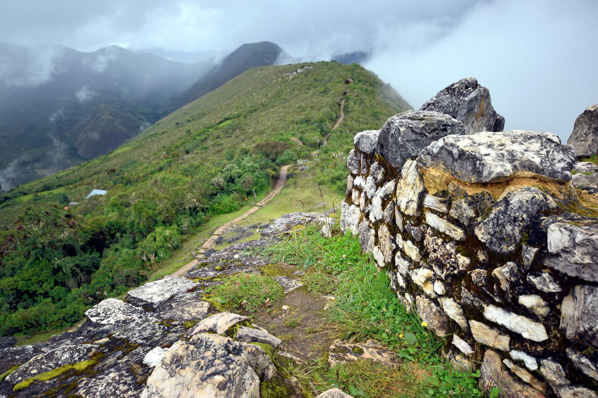 A massive stone wall running along a misty, forested mountain ridge