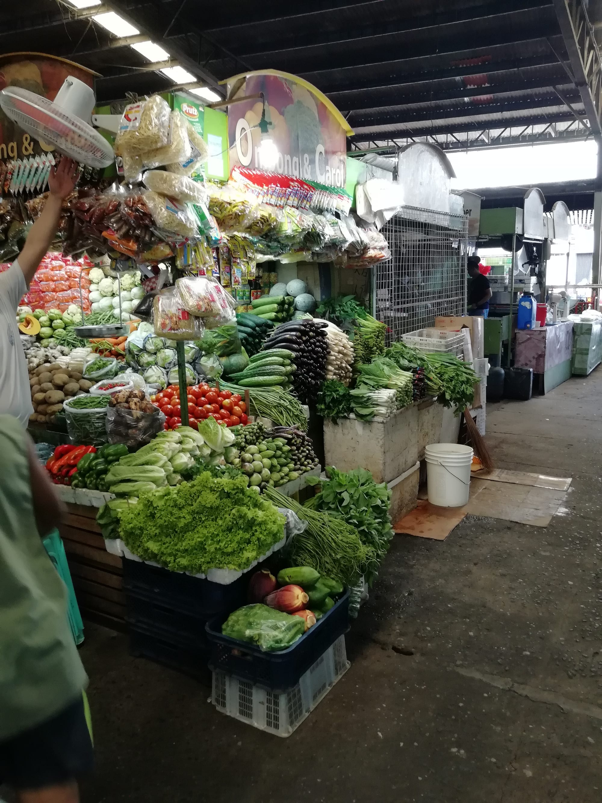 A covered wet market stall piled with fresh vegetables including tomatoes, cabbage, and leafy greens