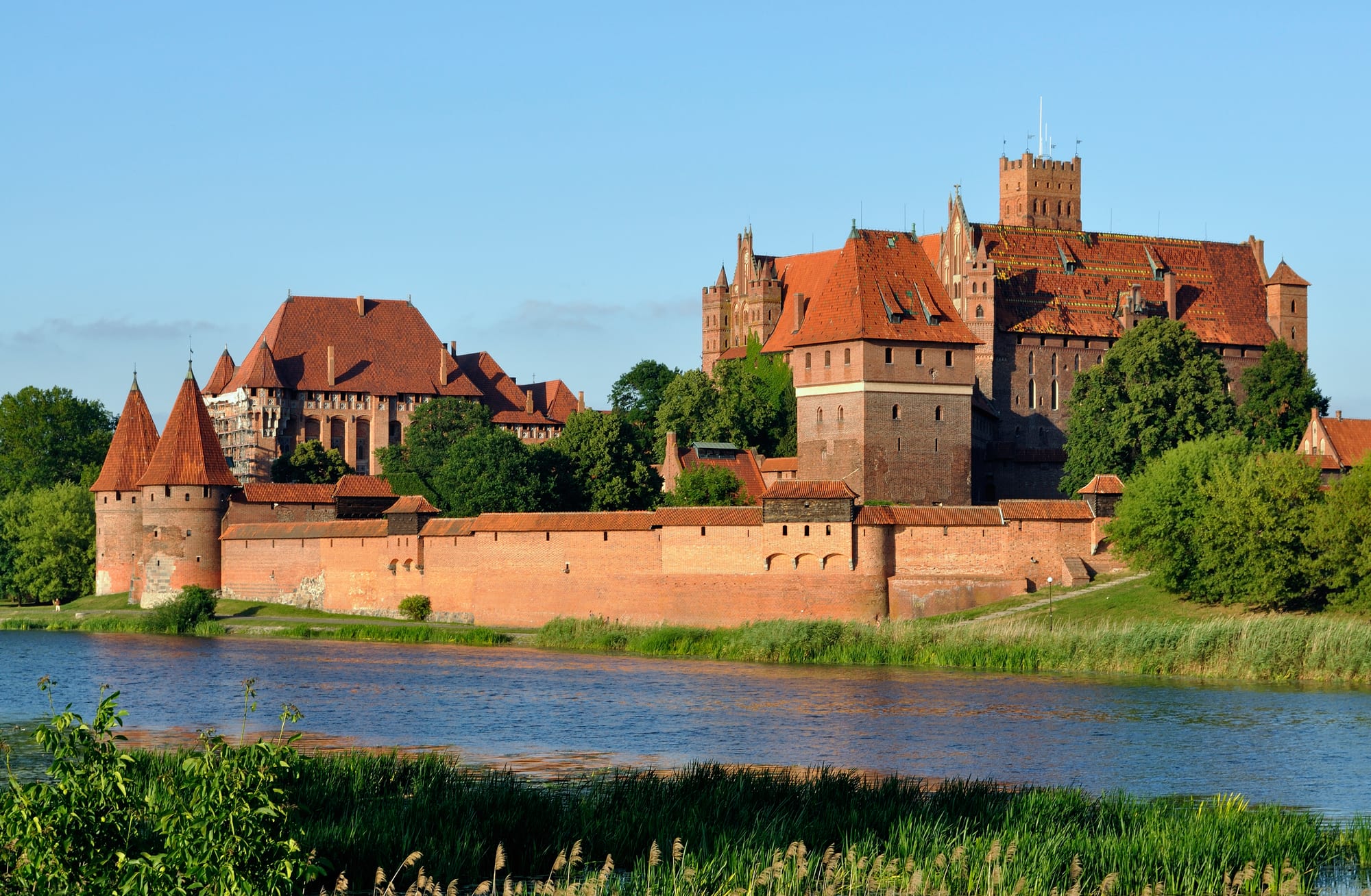 A massive red-brick medieval castle complex beside a river