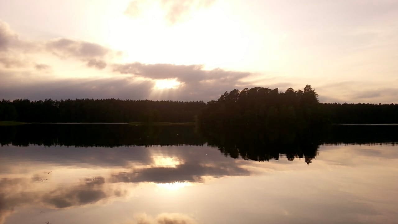 A calm lake reflecting a sunset and a dark tree-lined island