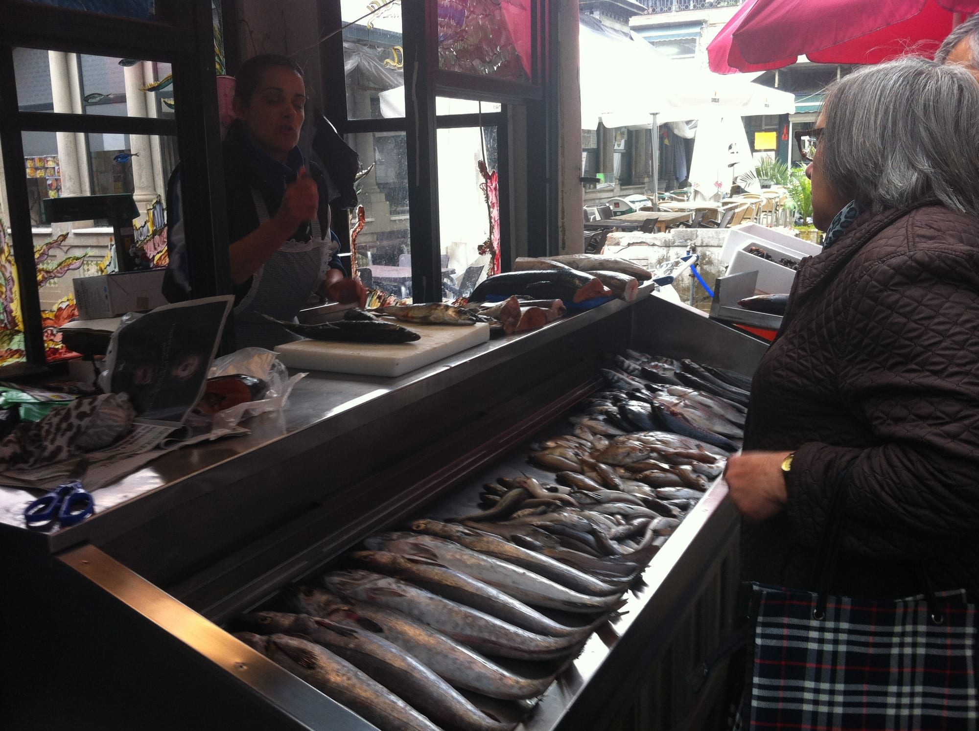 A woman being served at a fish stall piled with fresh whole fish, with a vendor behind the counter