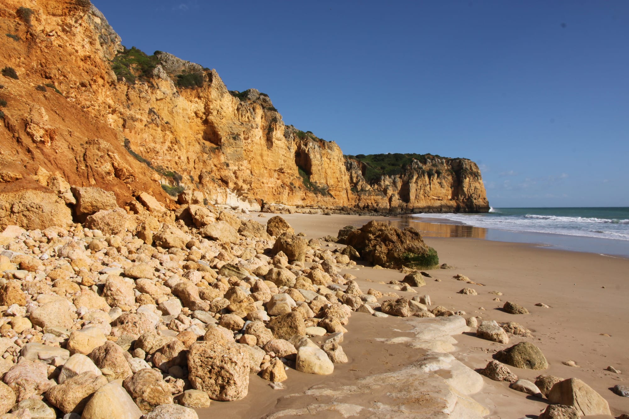 Golden limestone cliffs along a beach with clear turquoise water