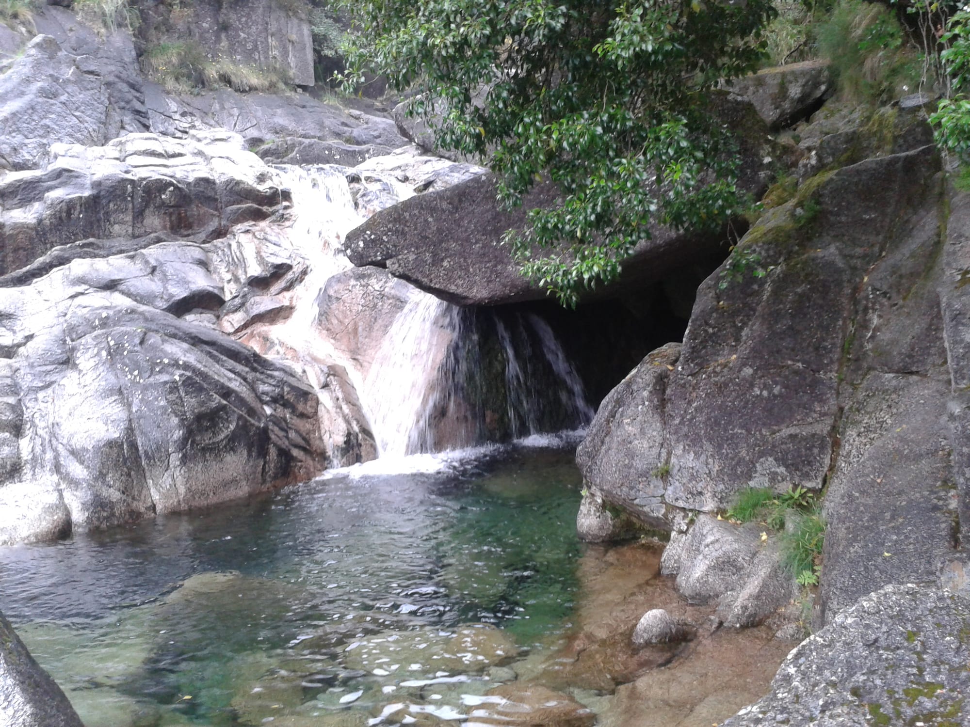 A waterfall spilling into a clear green pool among granite boulders