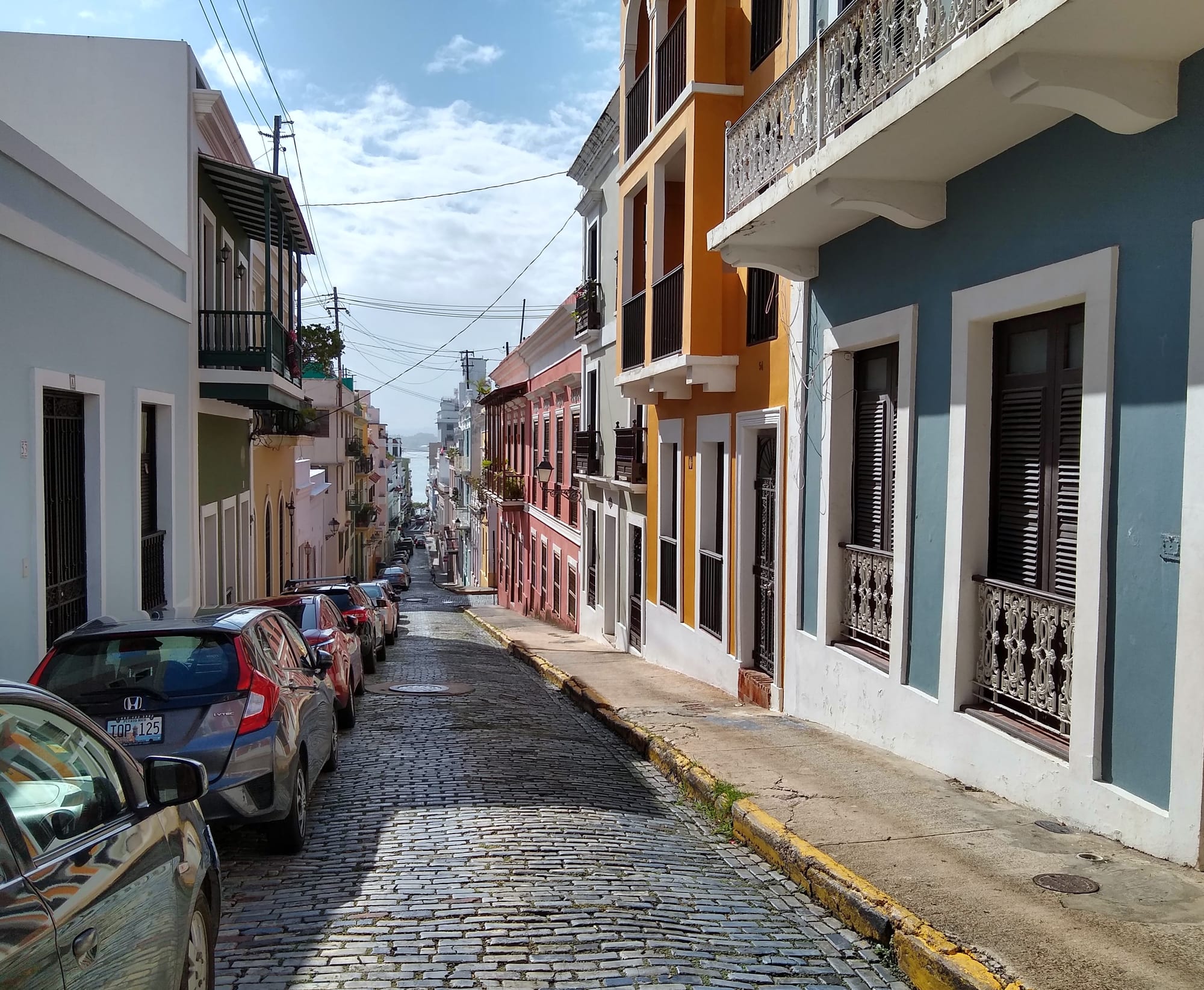 A narrow colonial street paved with blue-grey cobblestones lined with colourful buildings
