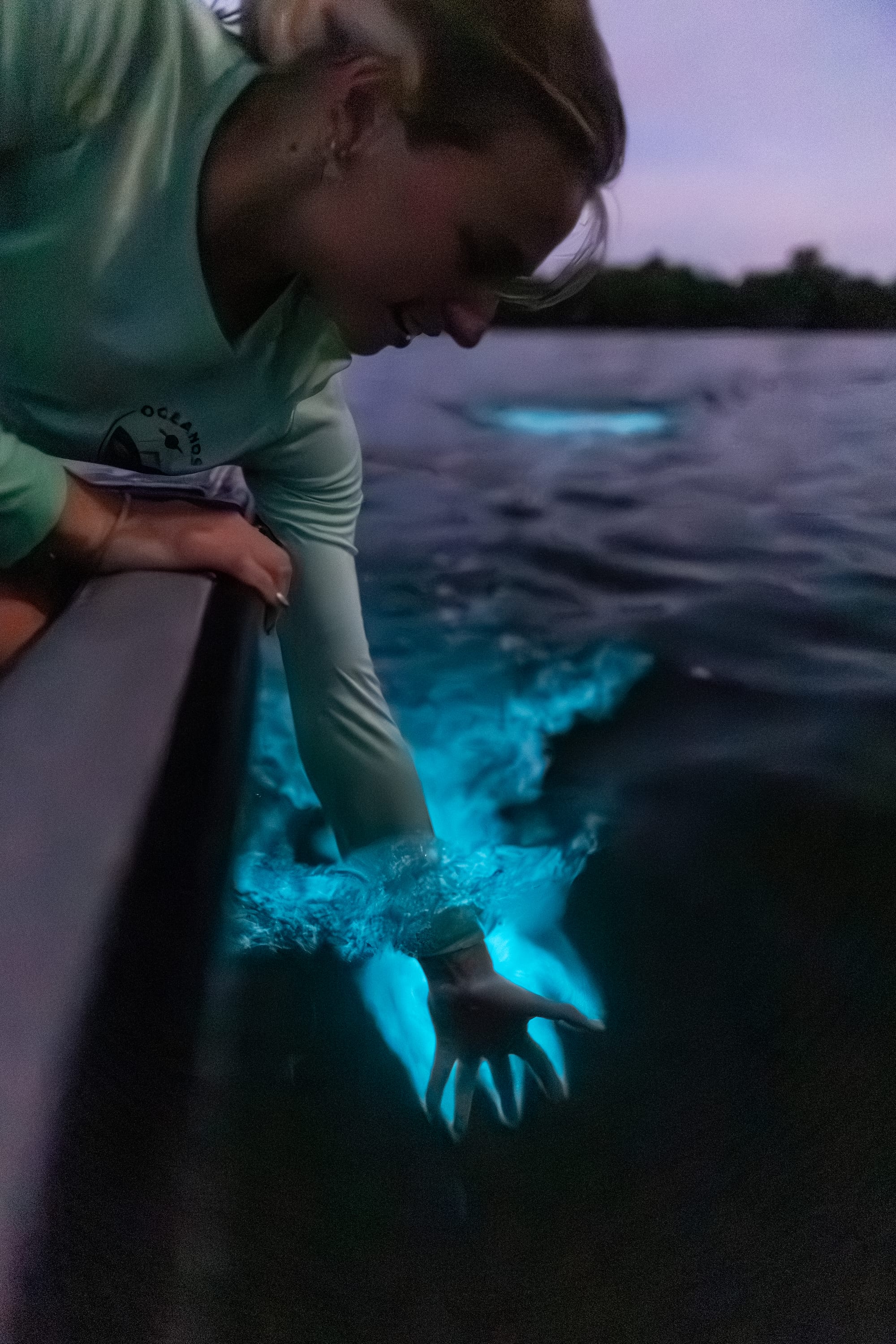 A hand glowing bright blue as it disturbs bioluminescent plankton in dark water