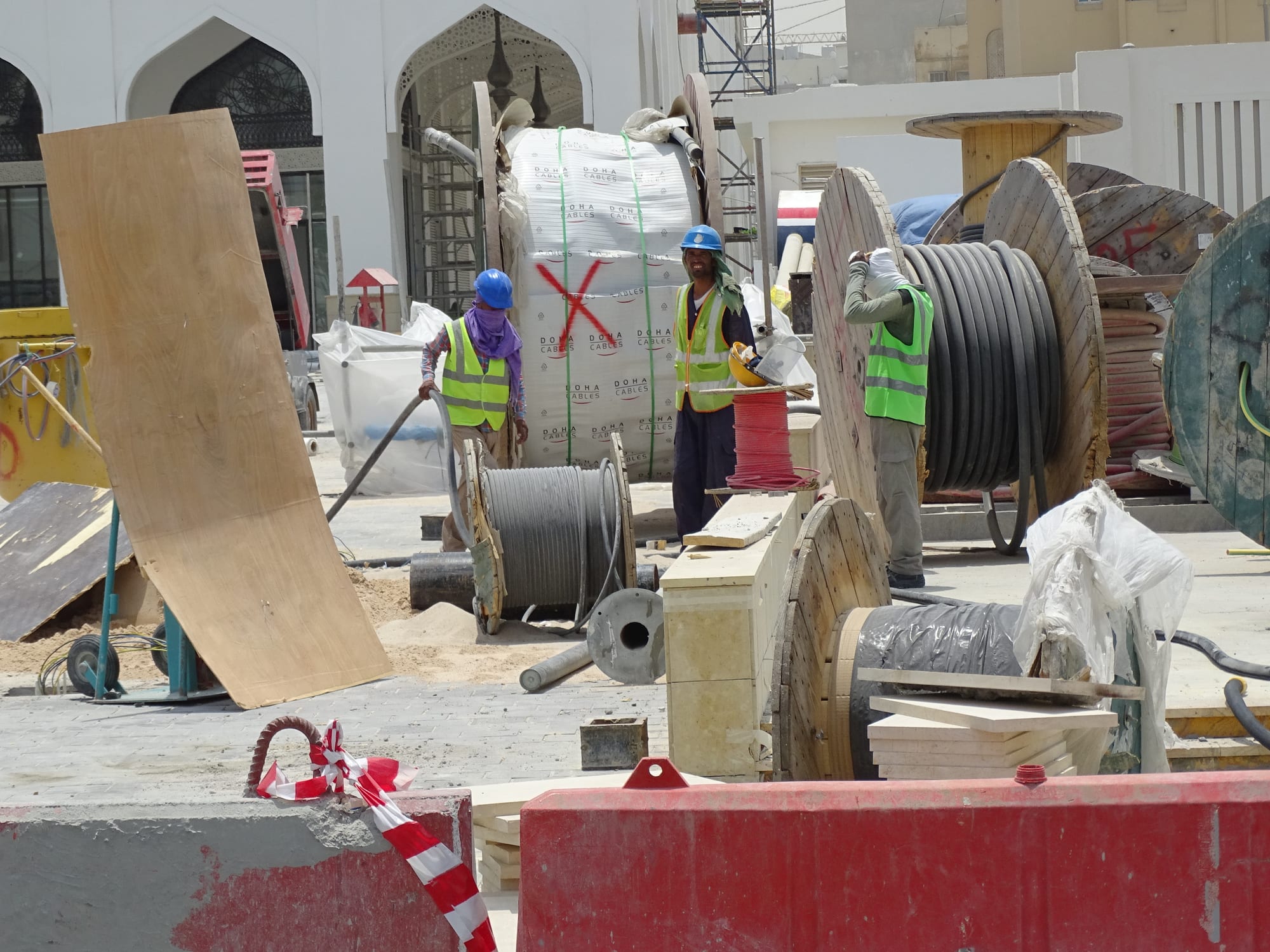 Three construction workers in hard hats and high-visibility vests working among large cable reels on a building site