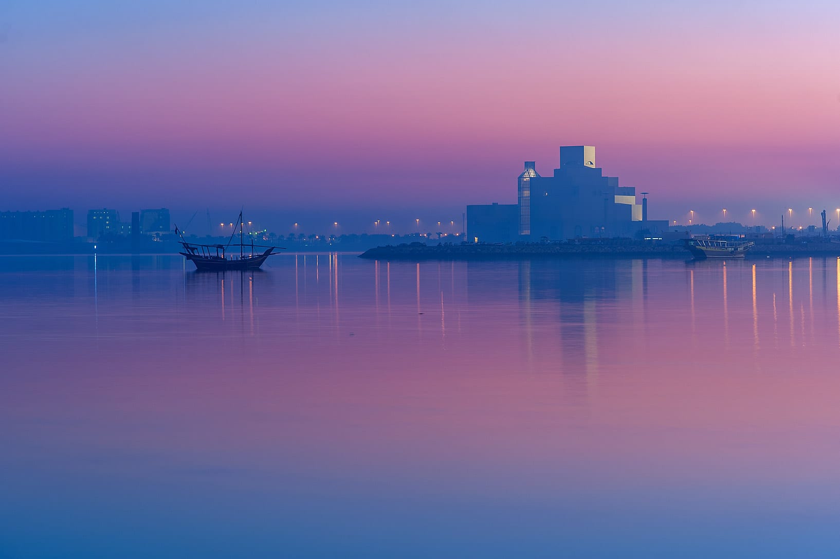 A geometric stone museum building beside the water at dusk