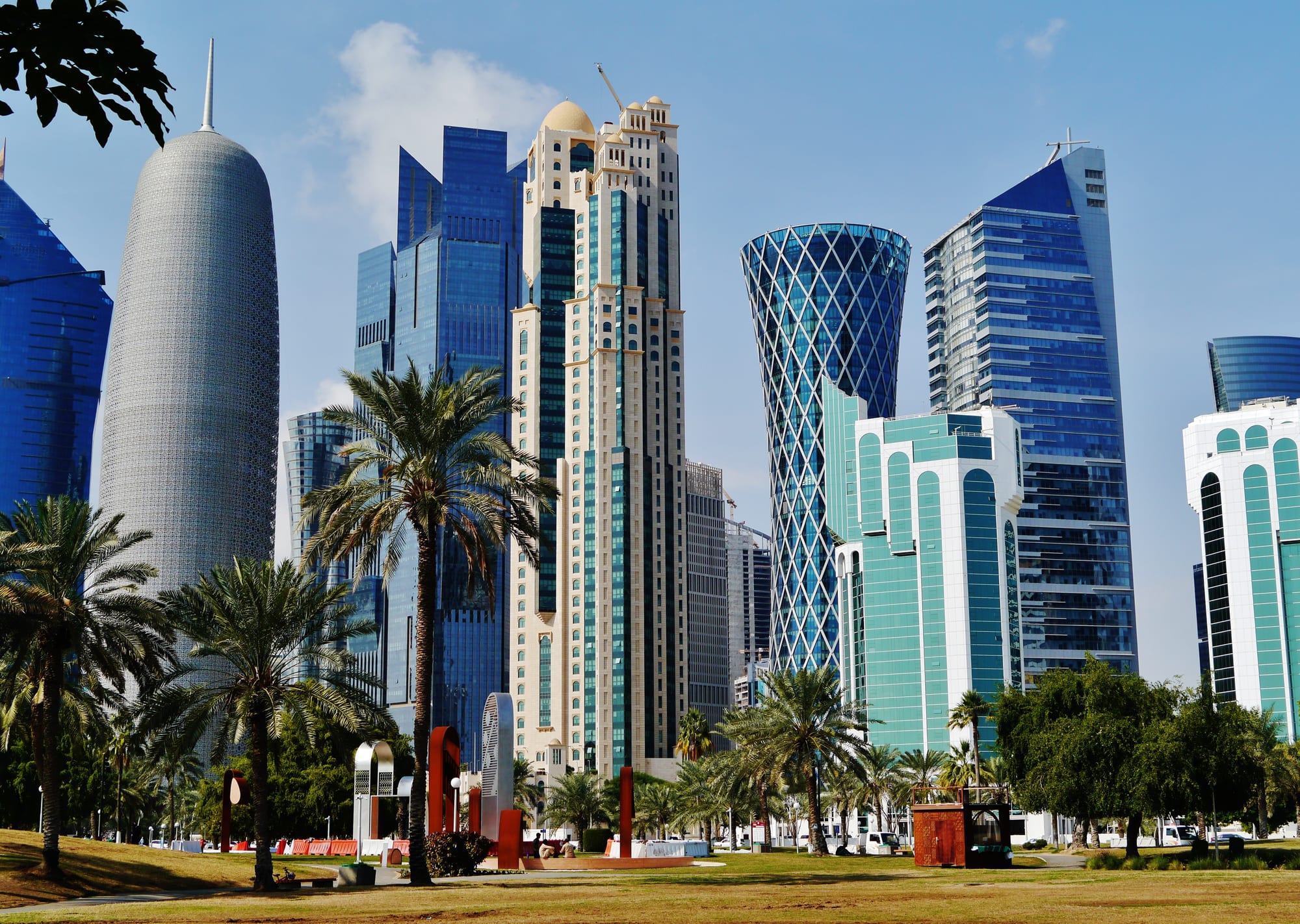 A dense cluster of modern towers of many shapes on the Doha waterfront under a hazy sky