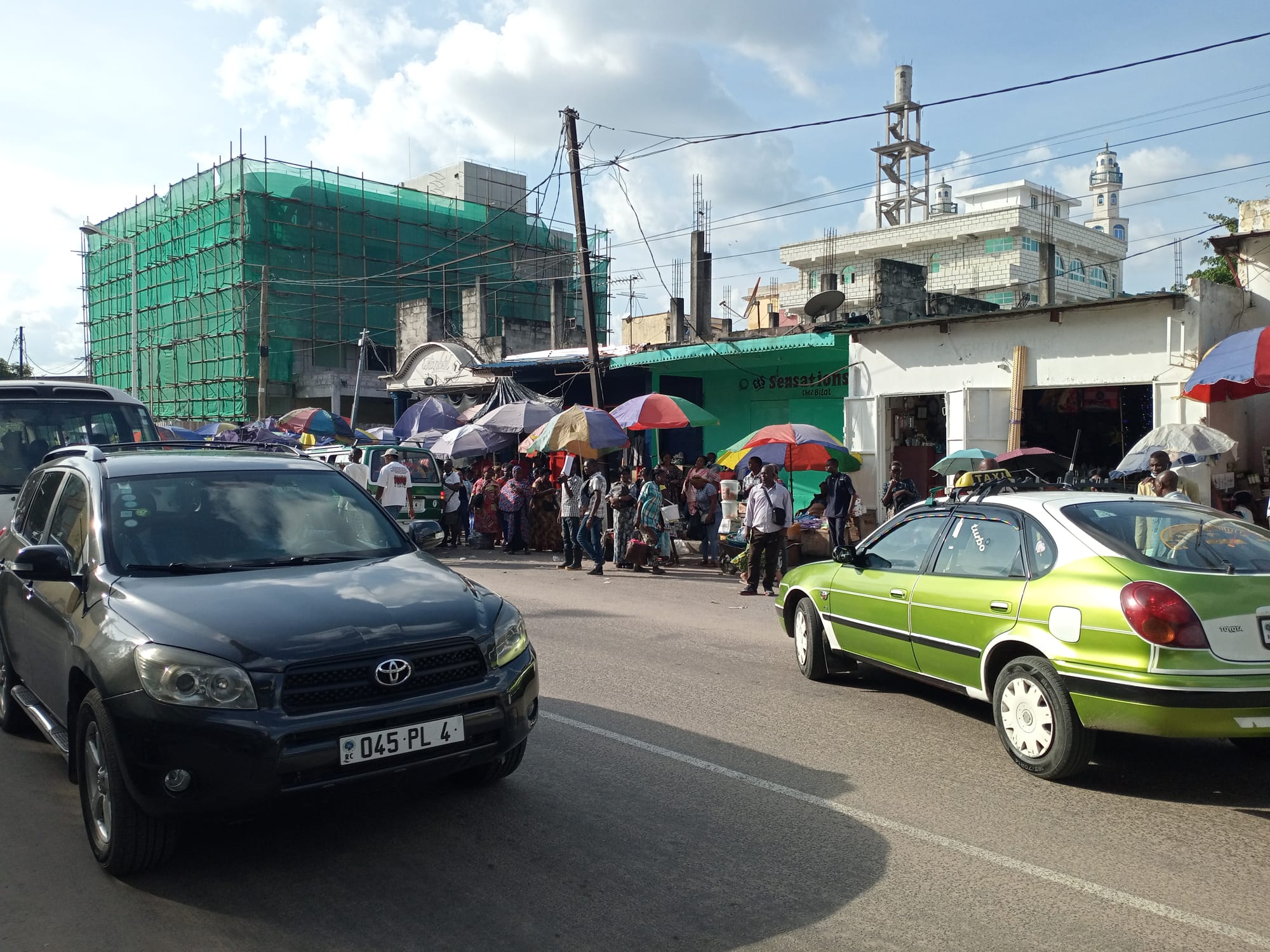 A busy Brazzaville street with cars, motorbikes and colourful market umbrellas in front of shops and an apartment building