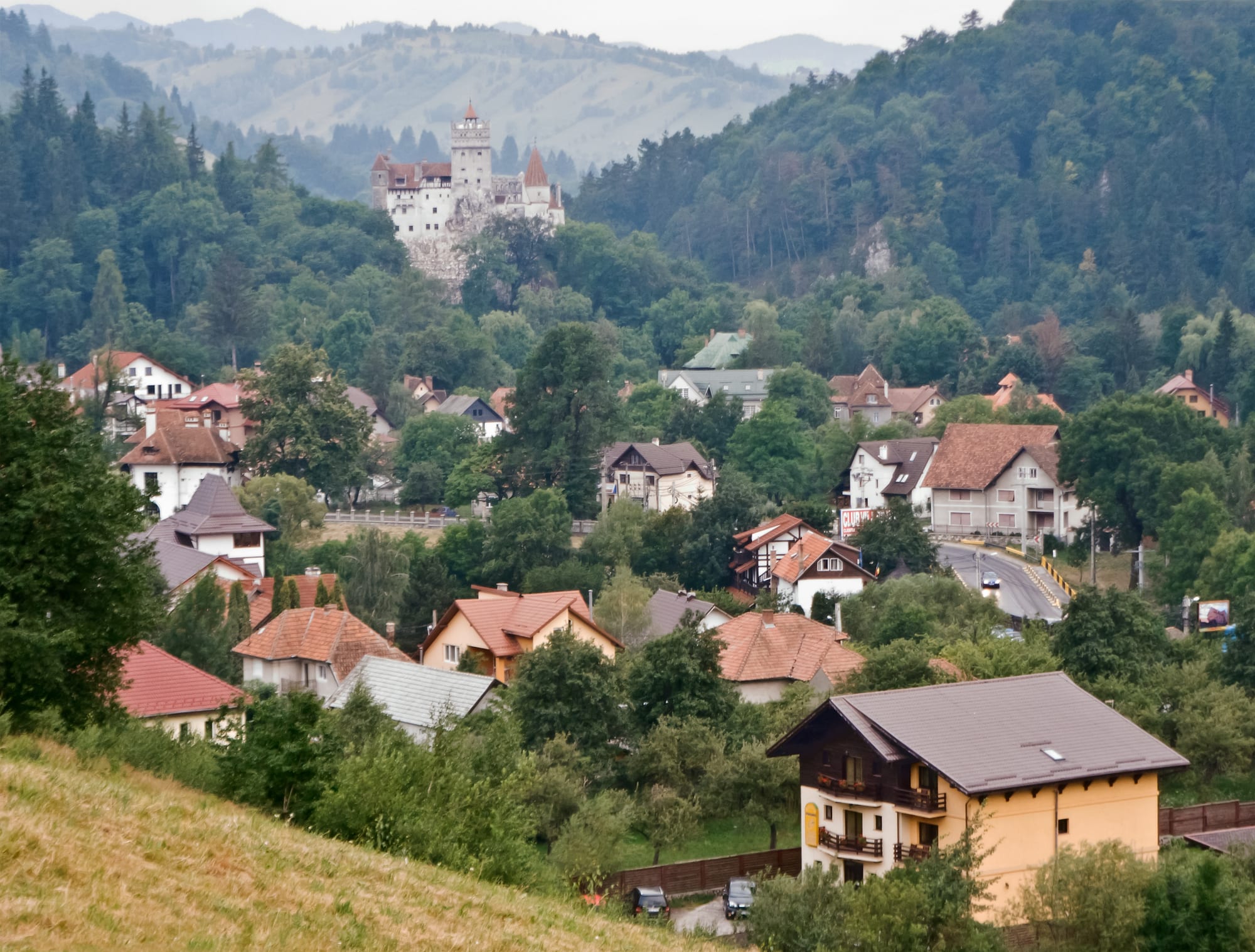 A tall castle perched on a rocky outcrop surrounded by forested hills
