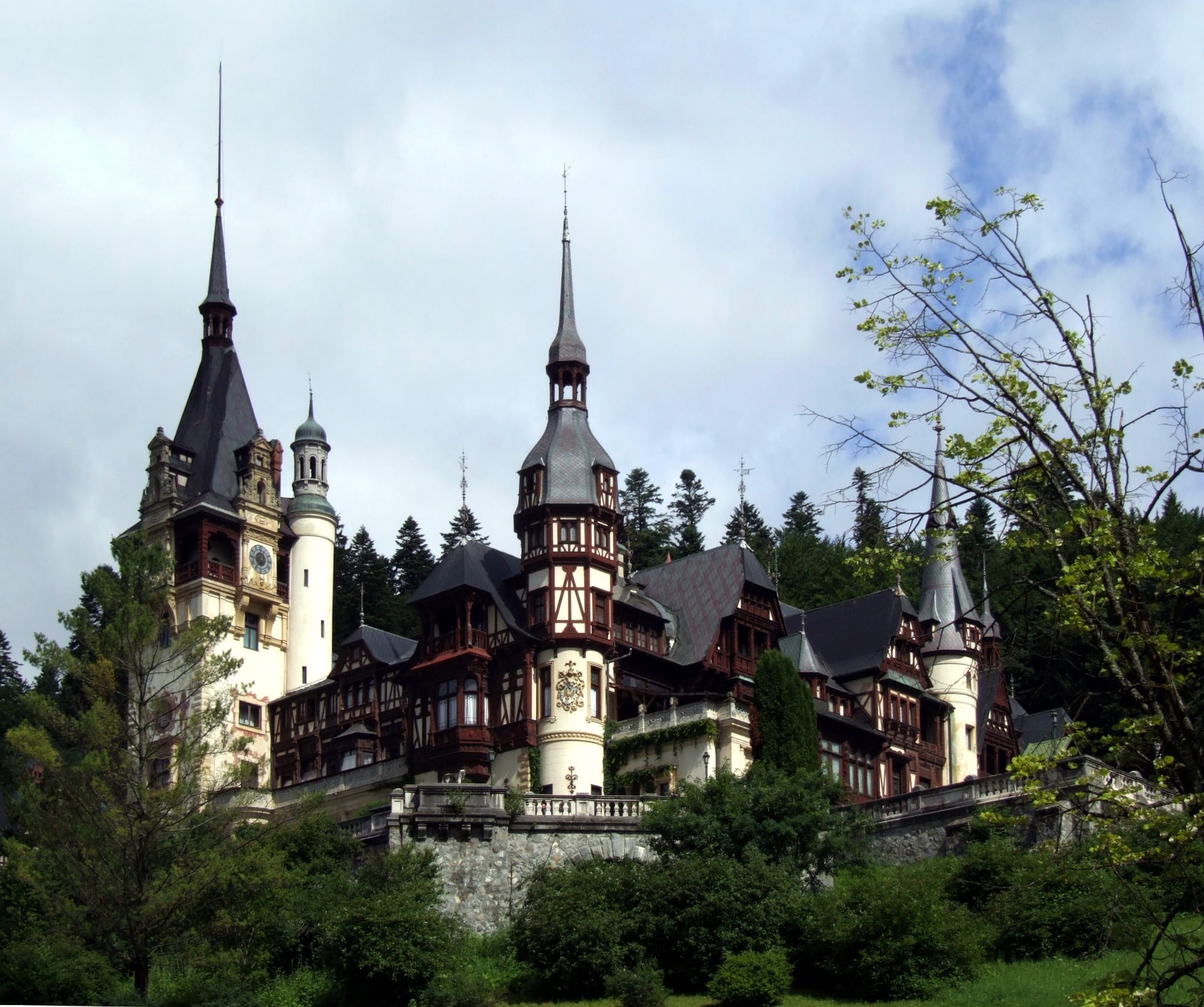 An ornate Neo-Renaissance castle with turrets set against a forested mountain backdrop