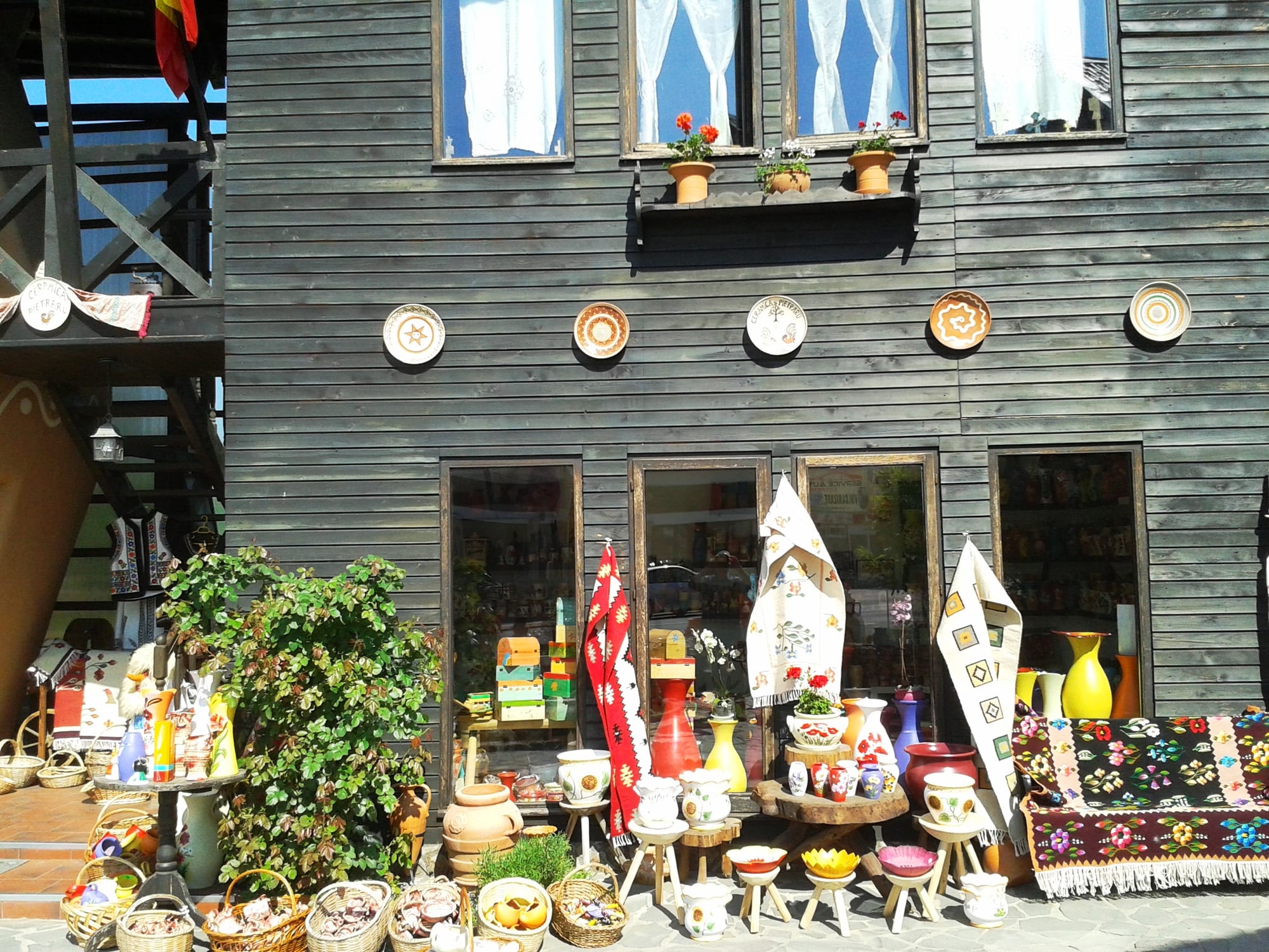 Decorated ceramic plates hung on the dark wooden wall of a house above a display of painted vases, jugs, bowls, baskets and a patterned woven rug