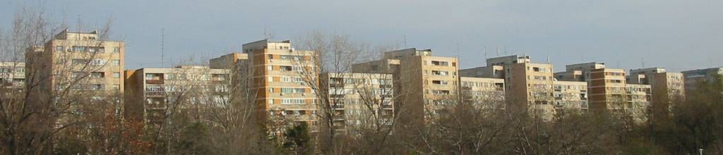 A row of tall concrete apartment blocks with balconies, seen across trees