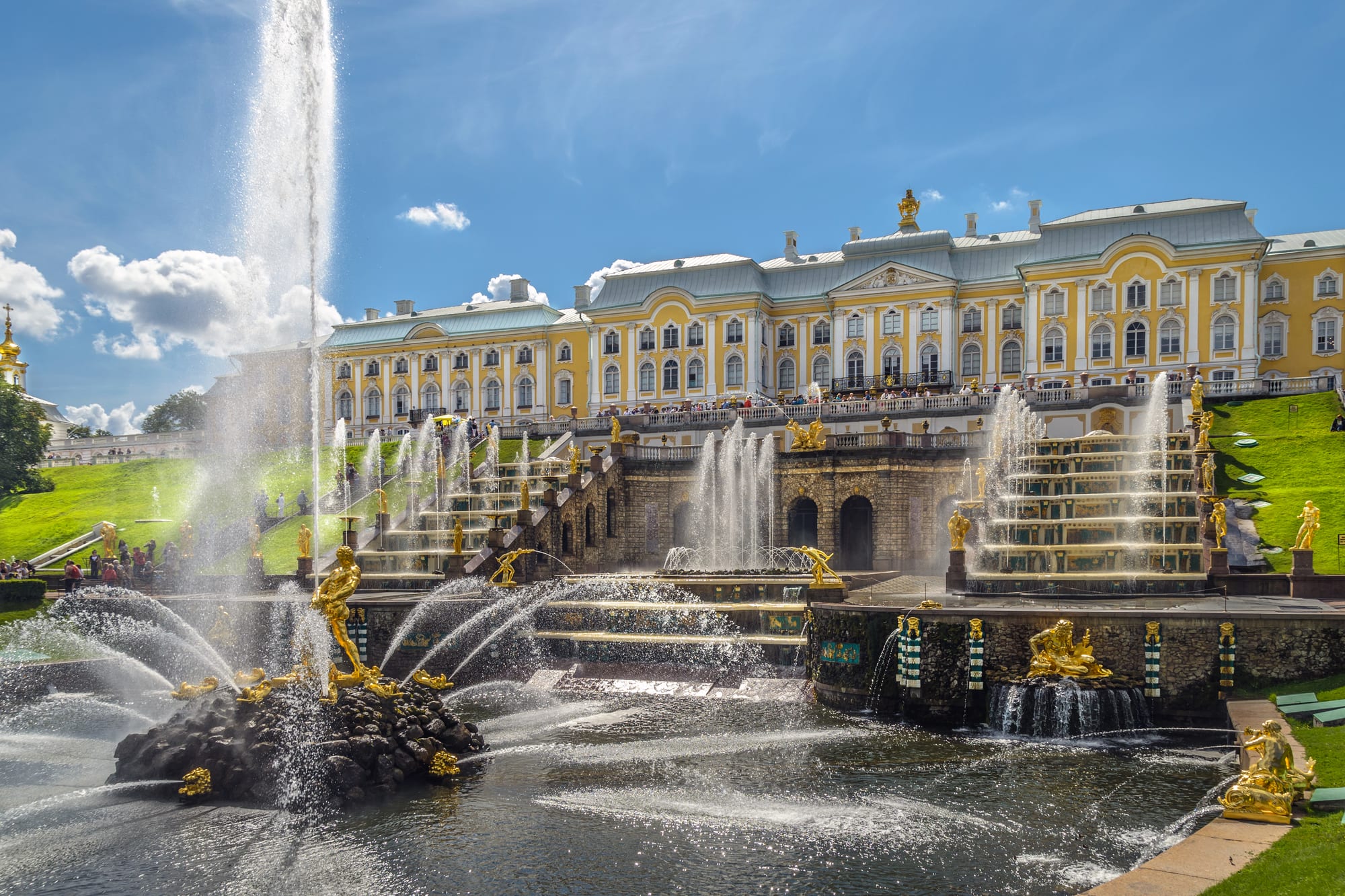 Golden statues and fountains cascading down steps in front of a yellow palace