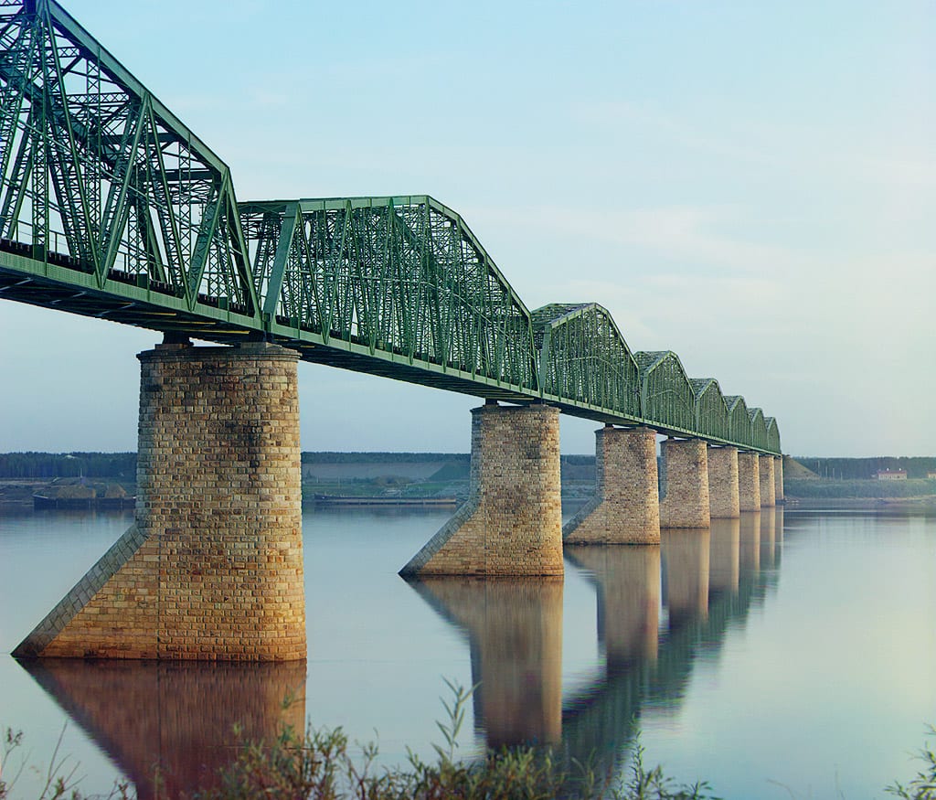 A historic iron railway bridge crossing a river in a forested landscape