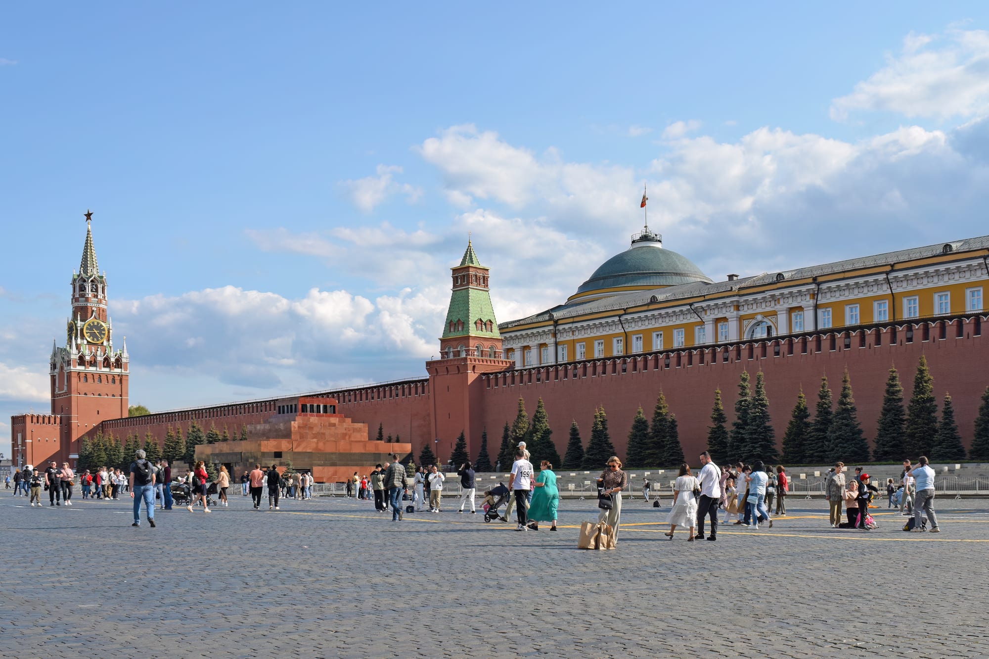 A grand red-brick fortress complex with towers beside a large public square